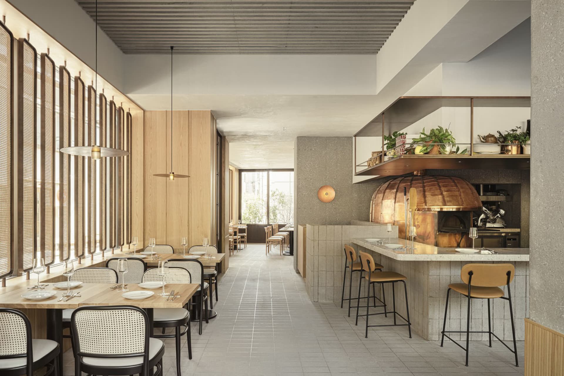 Modern restaurant interior with wooden tables, concrete walls, and a copper dome pizza oven.