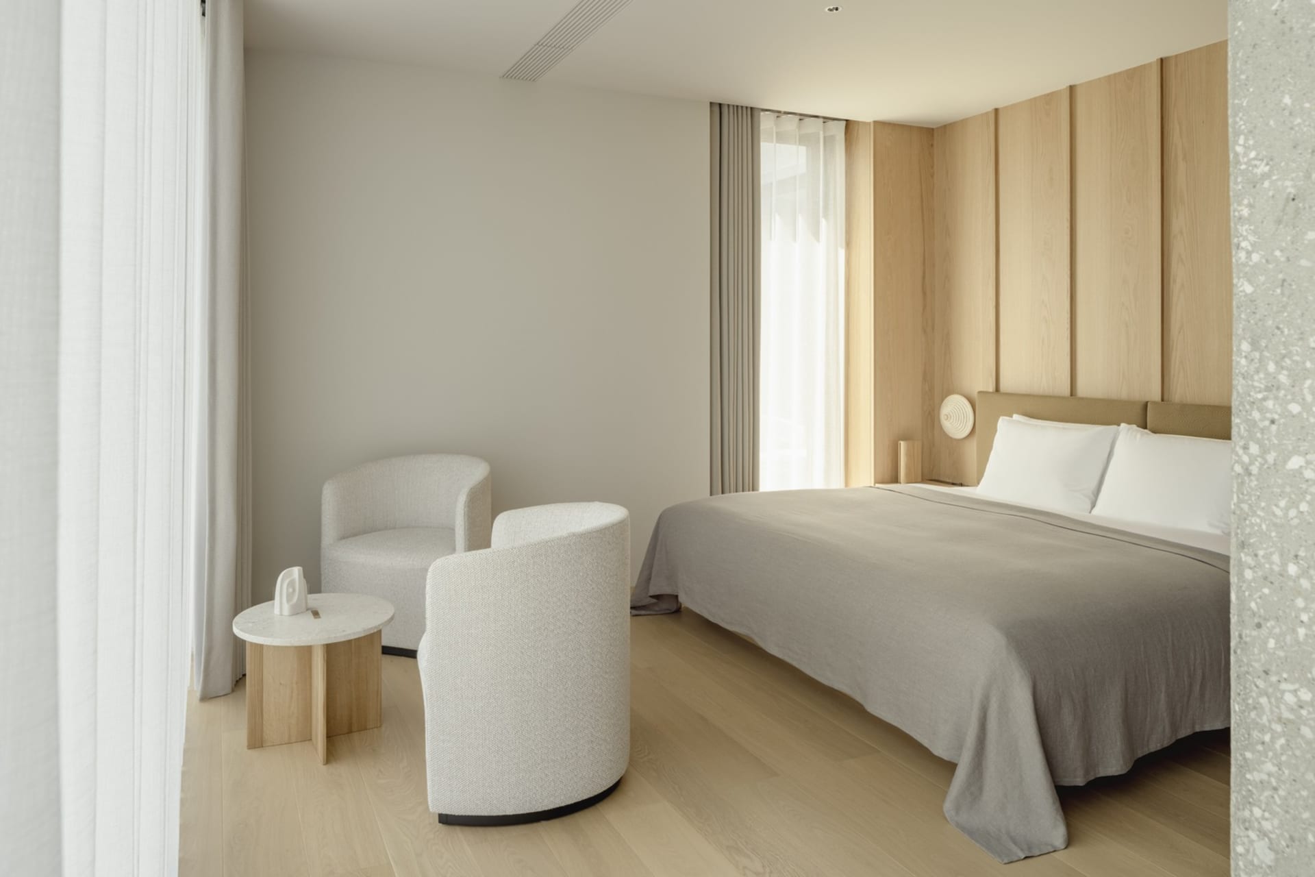A minimalist bedroom with a circular desk chair, a circular side table, and a bed with a white shade.