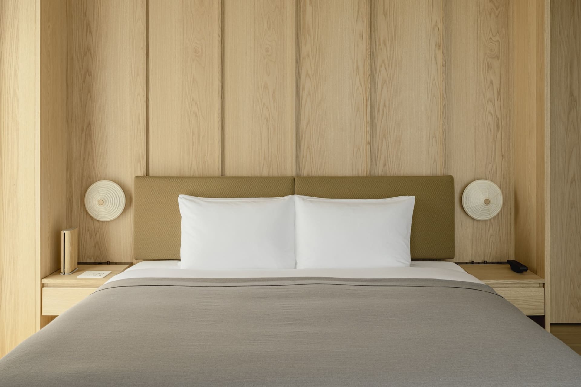 A minimalist bedroom with wood paneling and a neatly made bed.