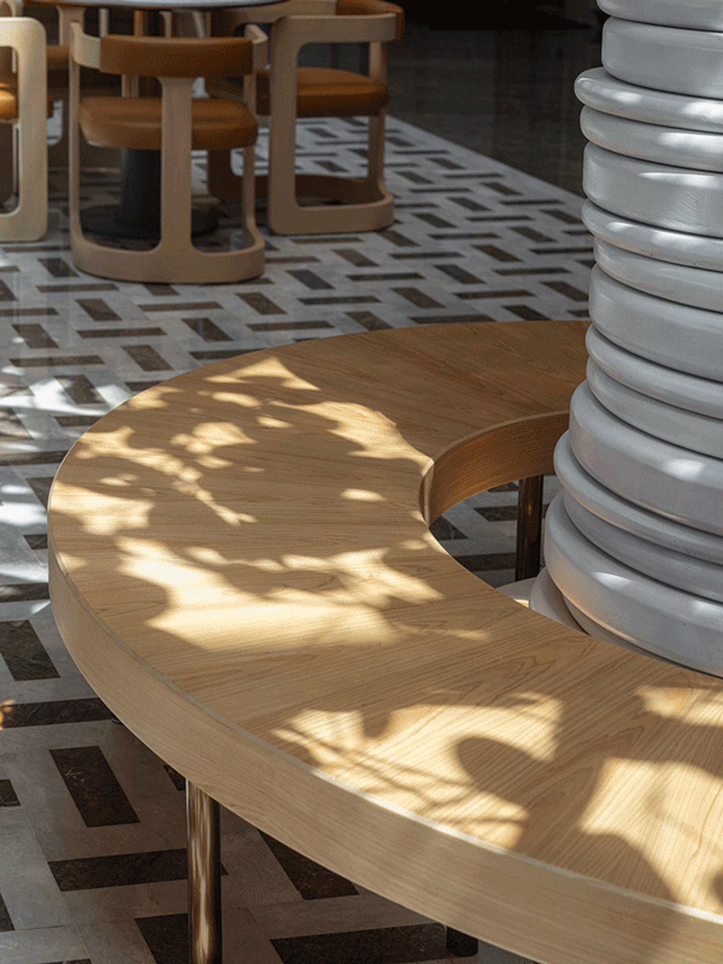 Modern interior design featuring a round wooden table with curved ends and a geometric patterned floor.