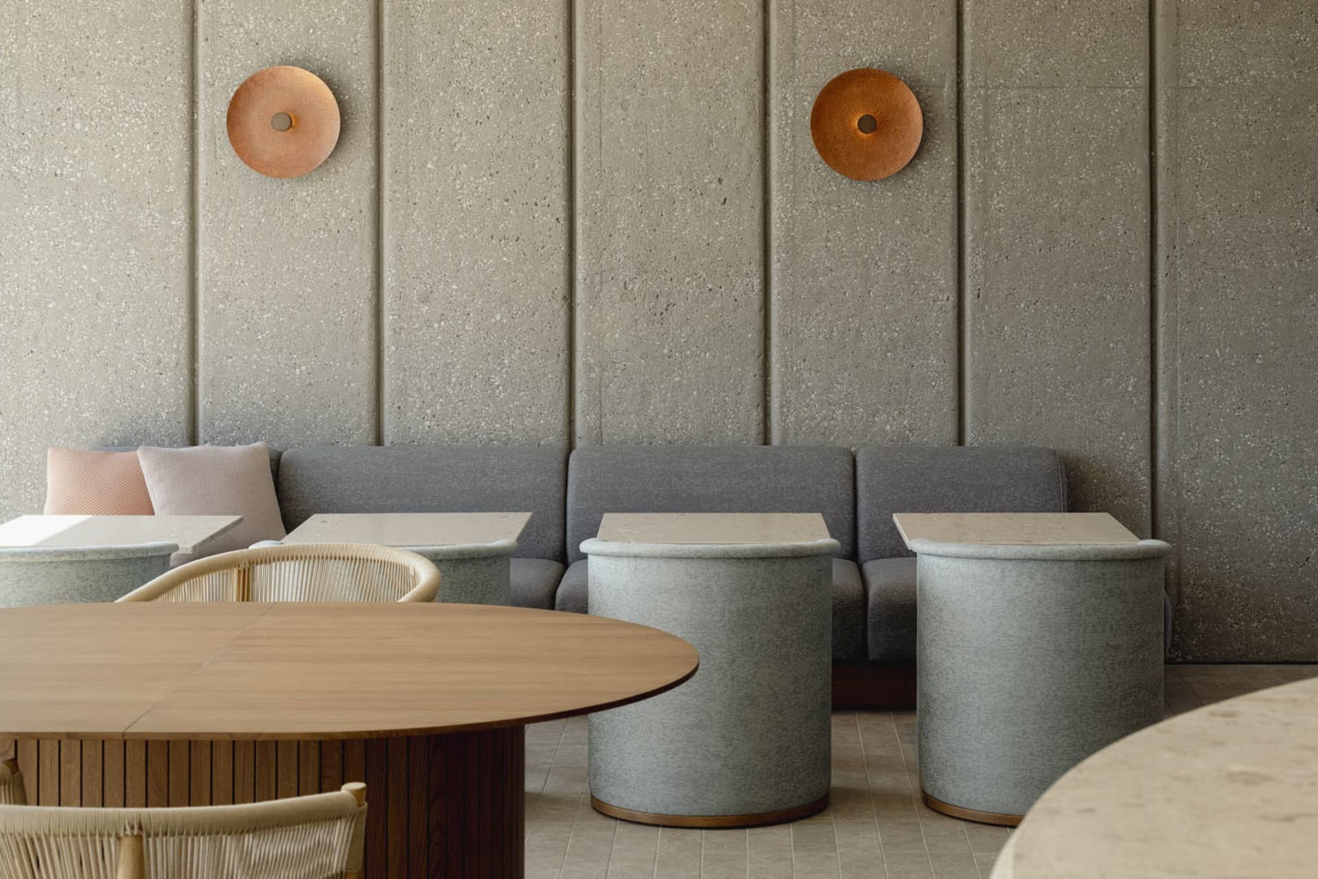Modern restaurant interior with concrete walls, fabric seating, and wooden tables and stools.