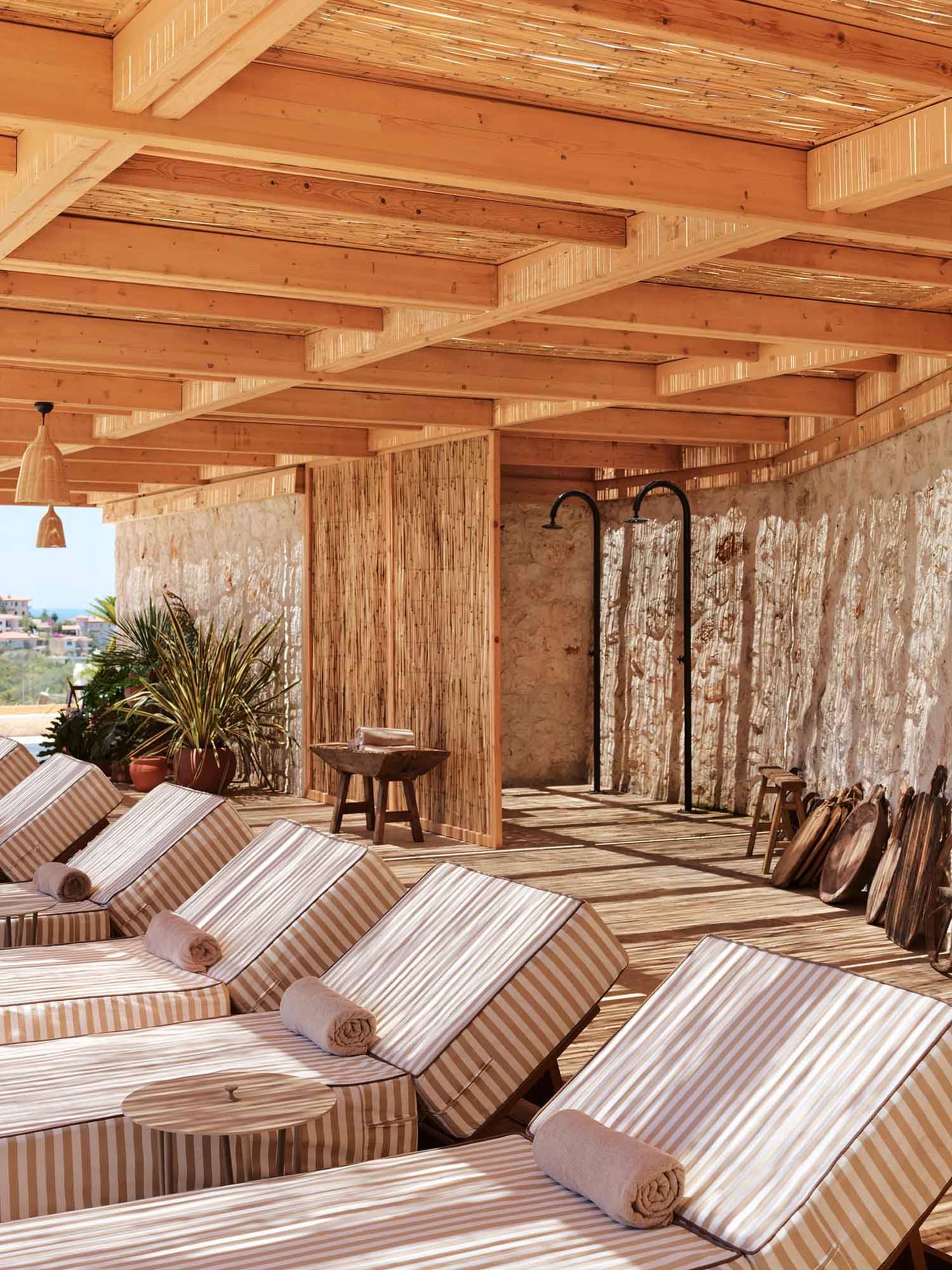 Spa setting with wooden and stone architecture, sunbeds, and shower areas.