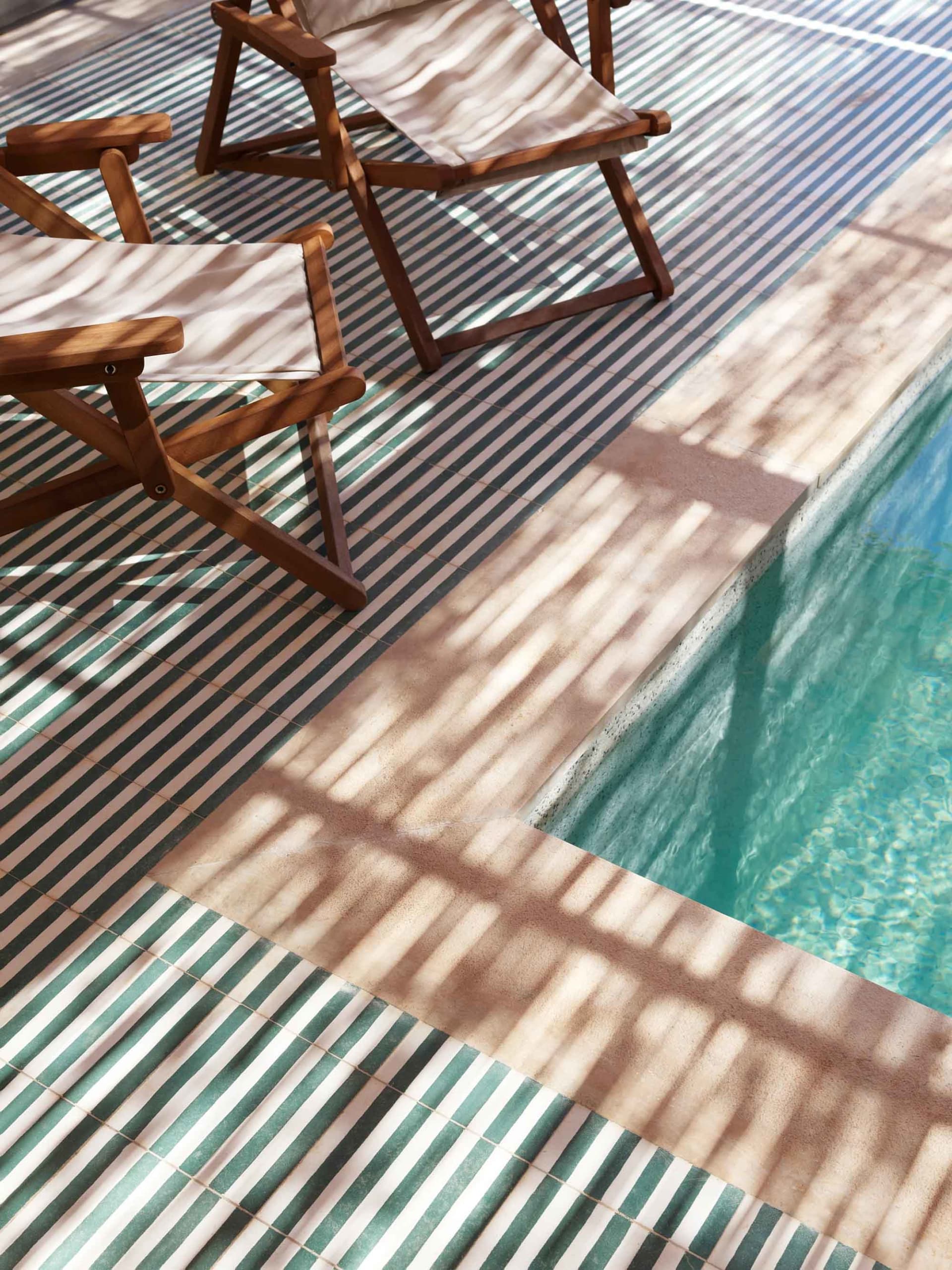 A poolside area with wooden and cement tiles under direct sunlight, creating sharp shadows.