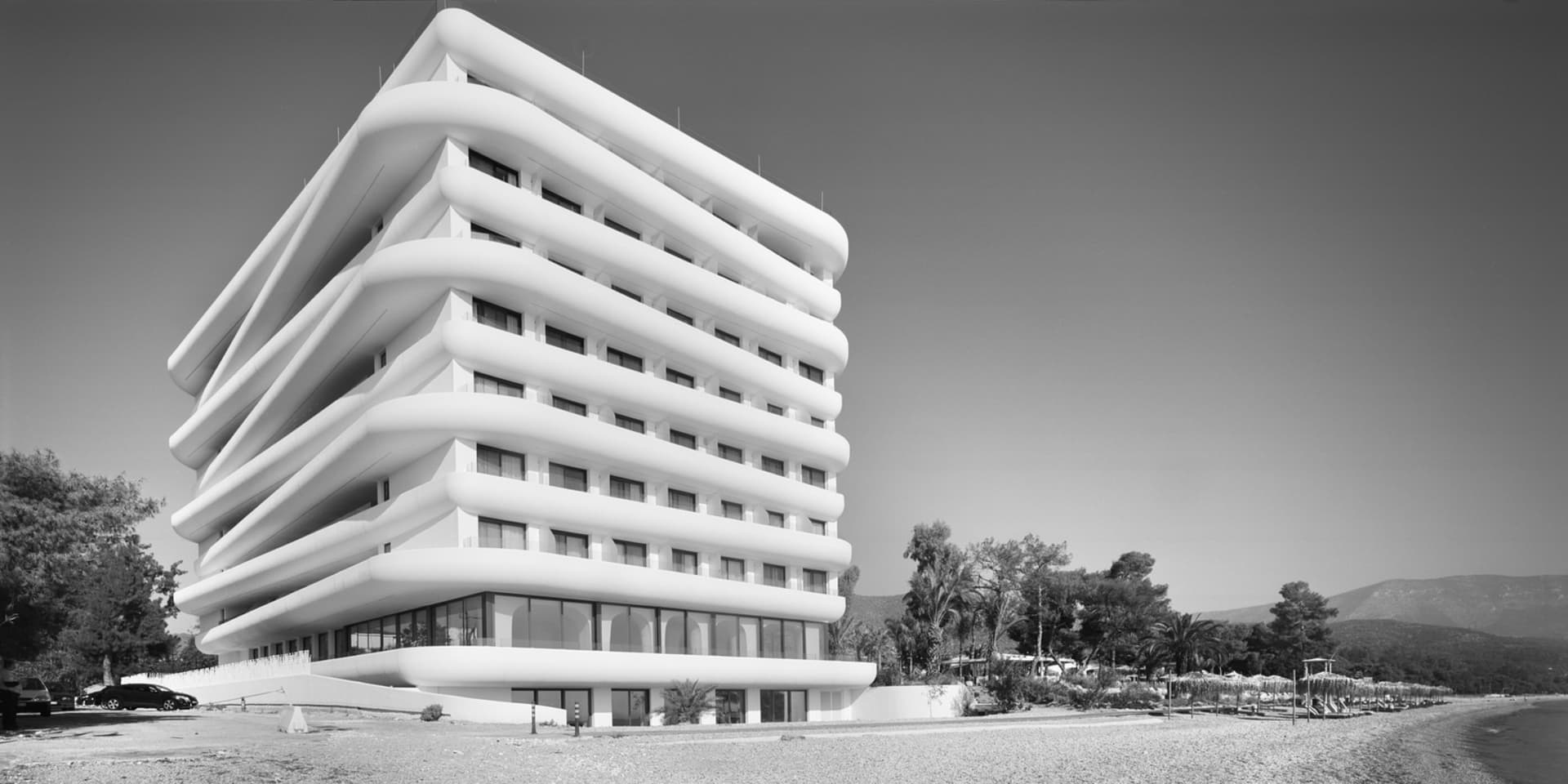 A modern, multi-storied building with curved balconies on a beachfront setting.