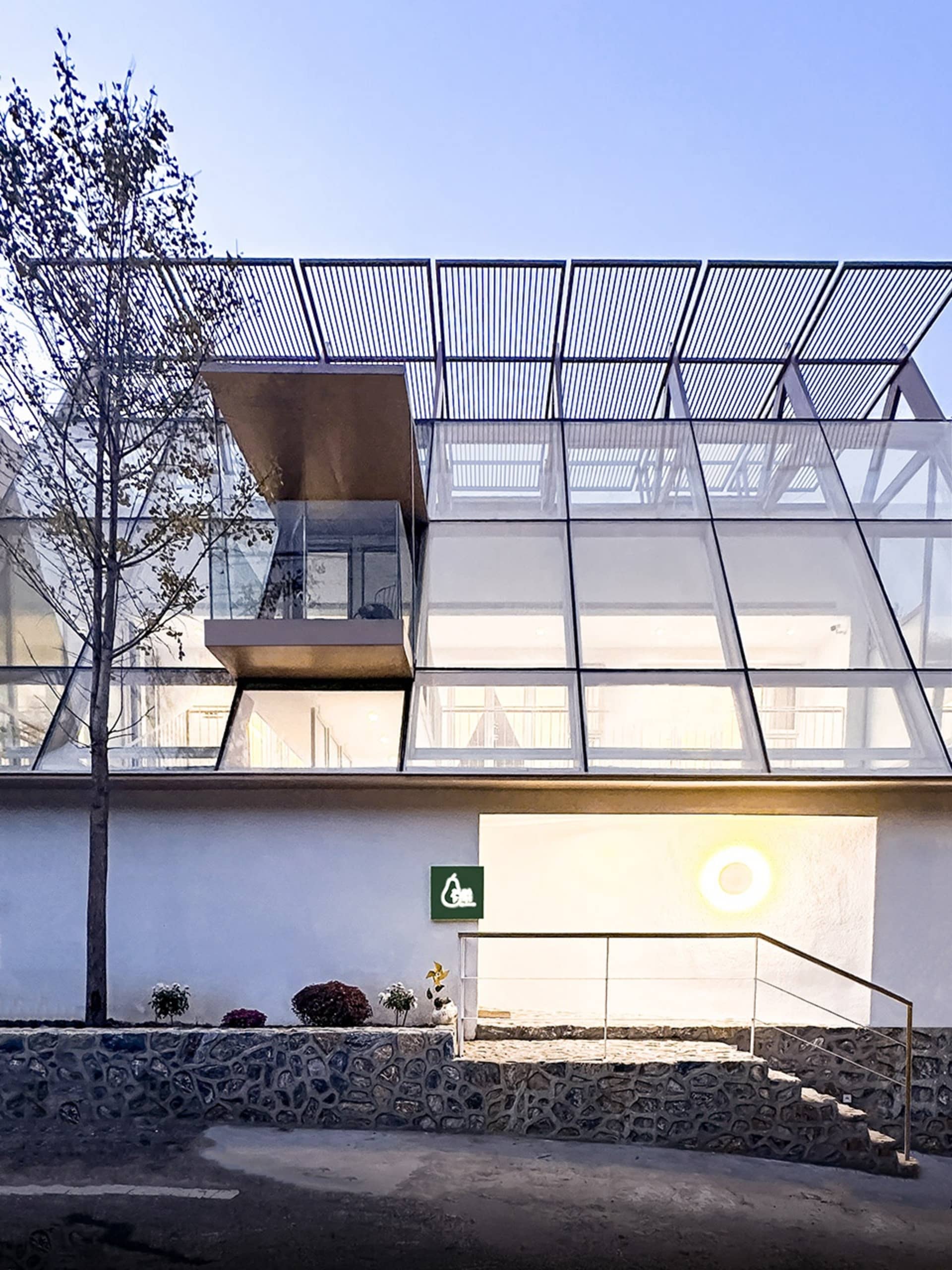 A modern residential building with a glass exterior and a metal lattice roof, featuring a stone staircase leading to an entra