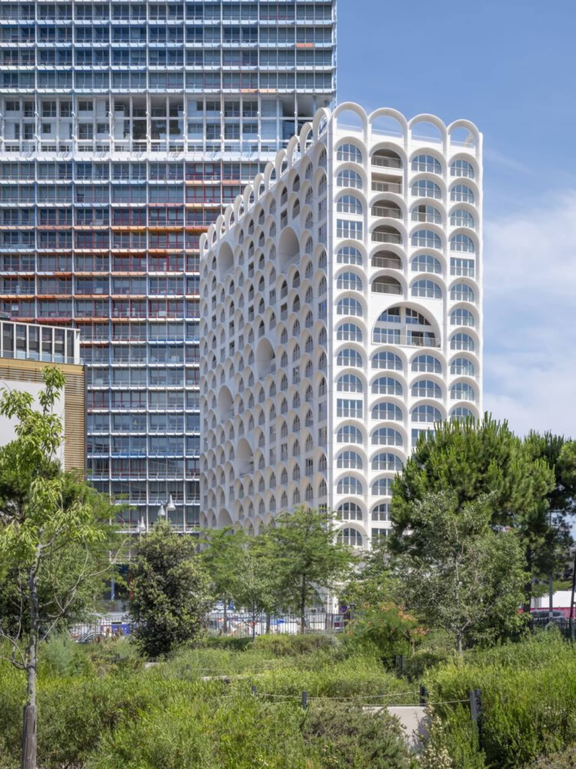 Modern apartment building with white stone facade and arched balconies against a blue sky.