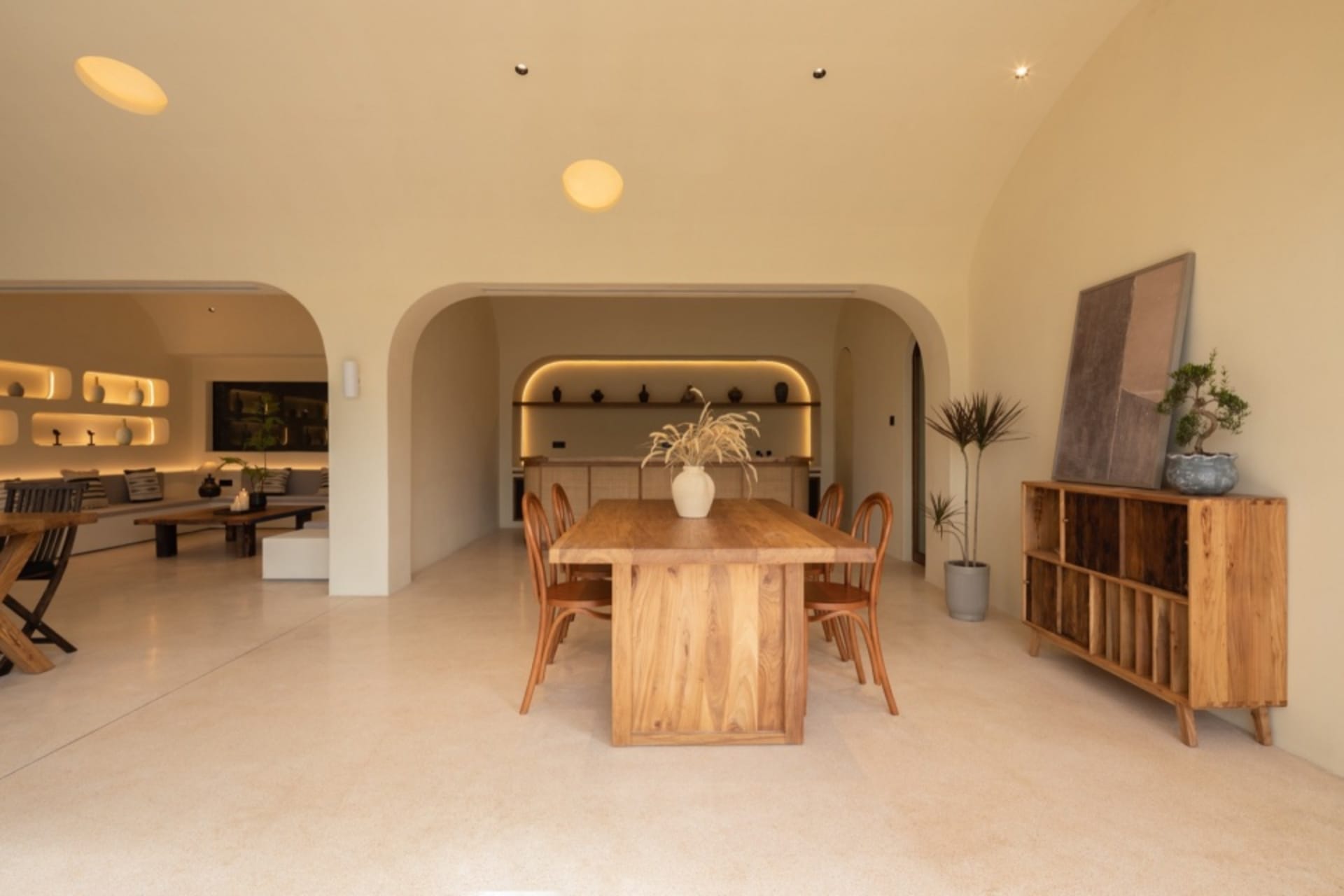 A modern interior design featuring a wooden living room with a long wooden table and chairs, potted plants, and archways.