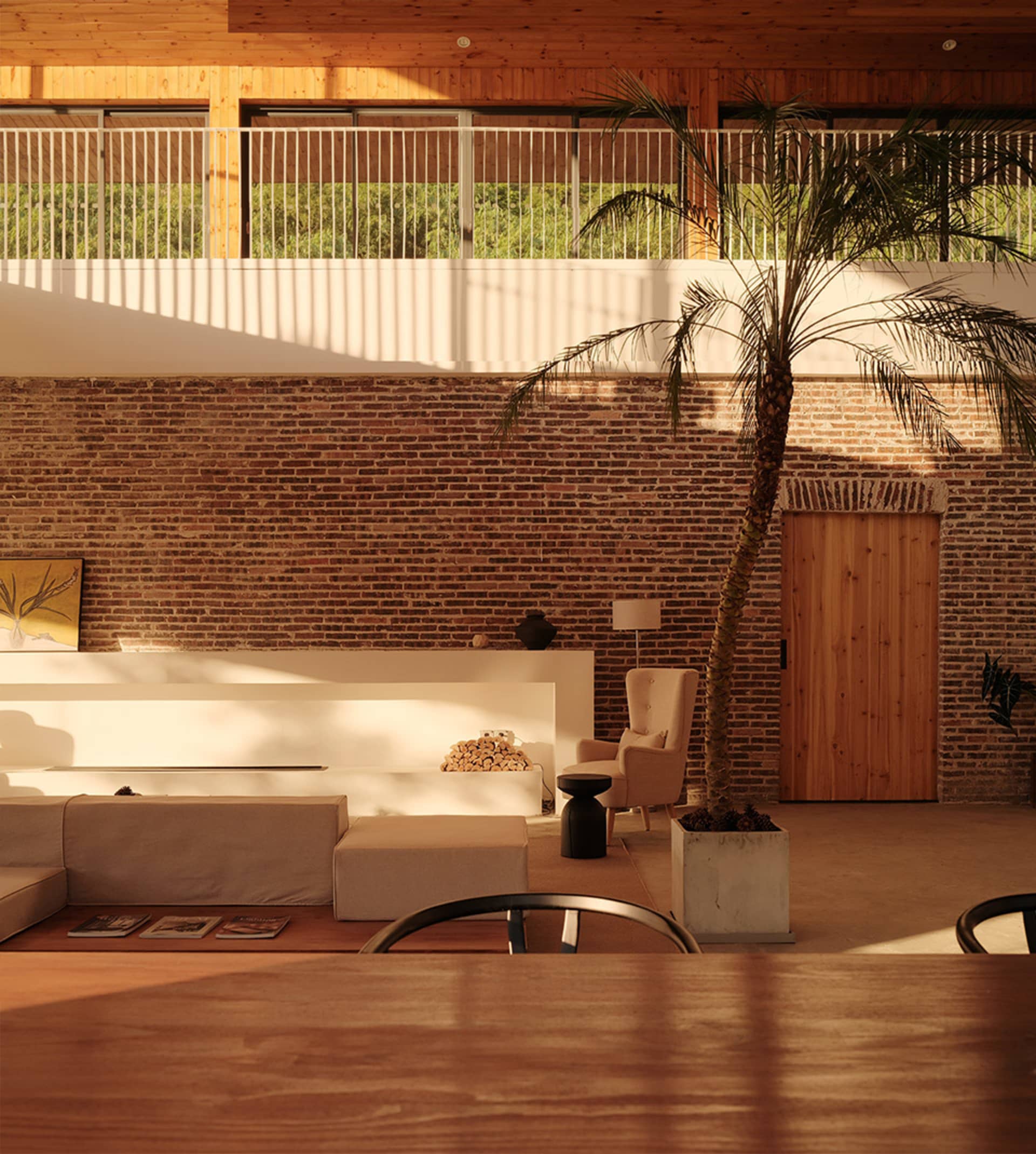A modern living room with exposed brick walls, wooden furniture, and a potted palm plant.