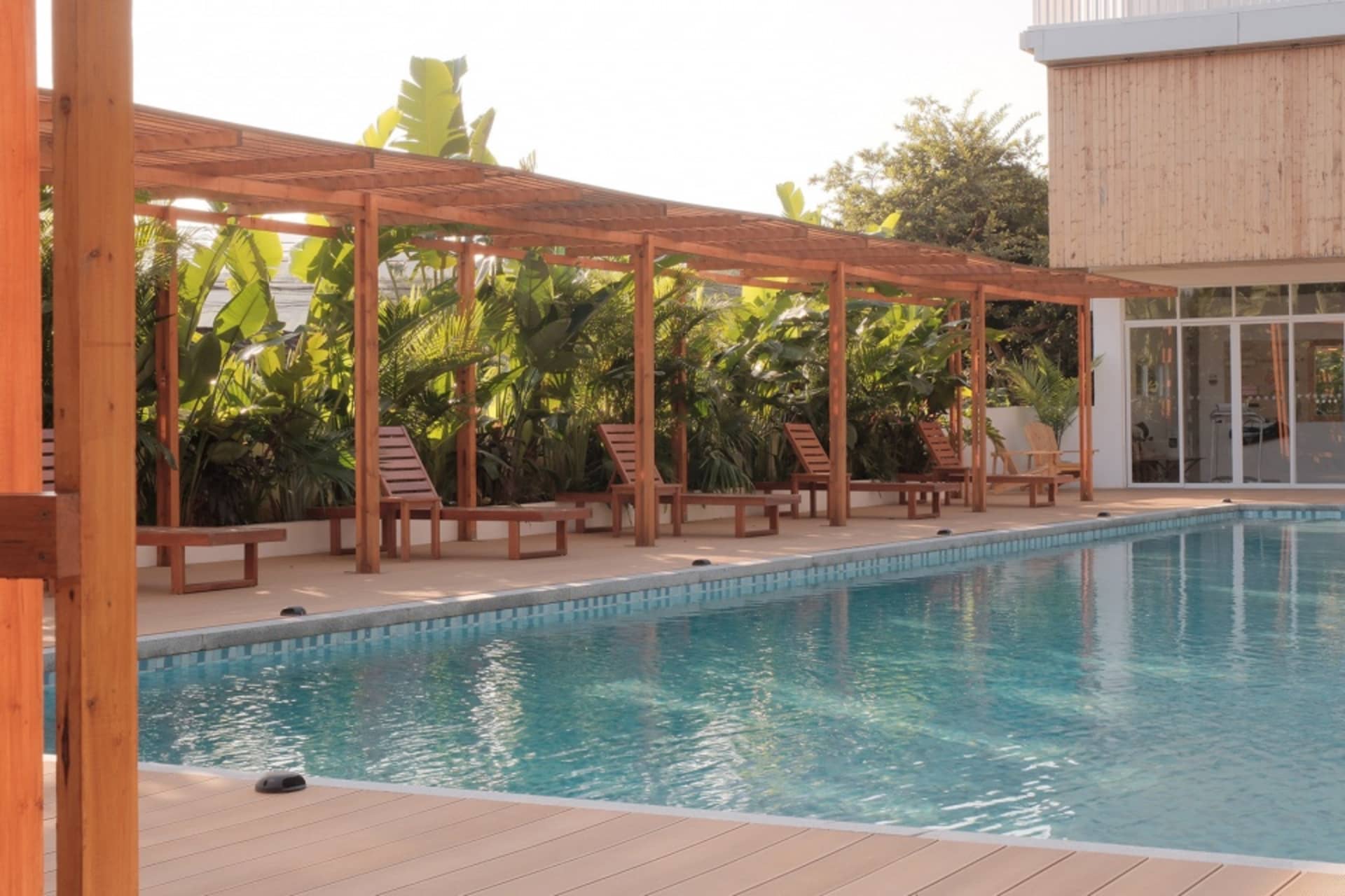 A residential poolside area featuring wooden pergola and lounge chairs surrounded by lush vegetation.