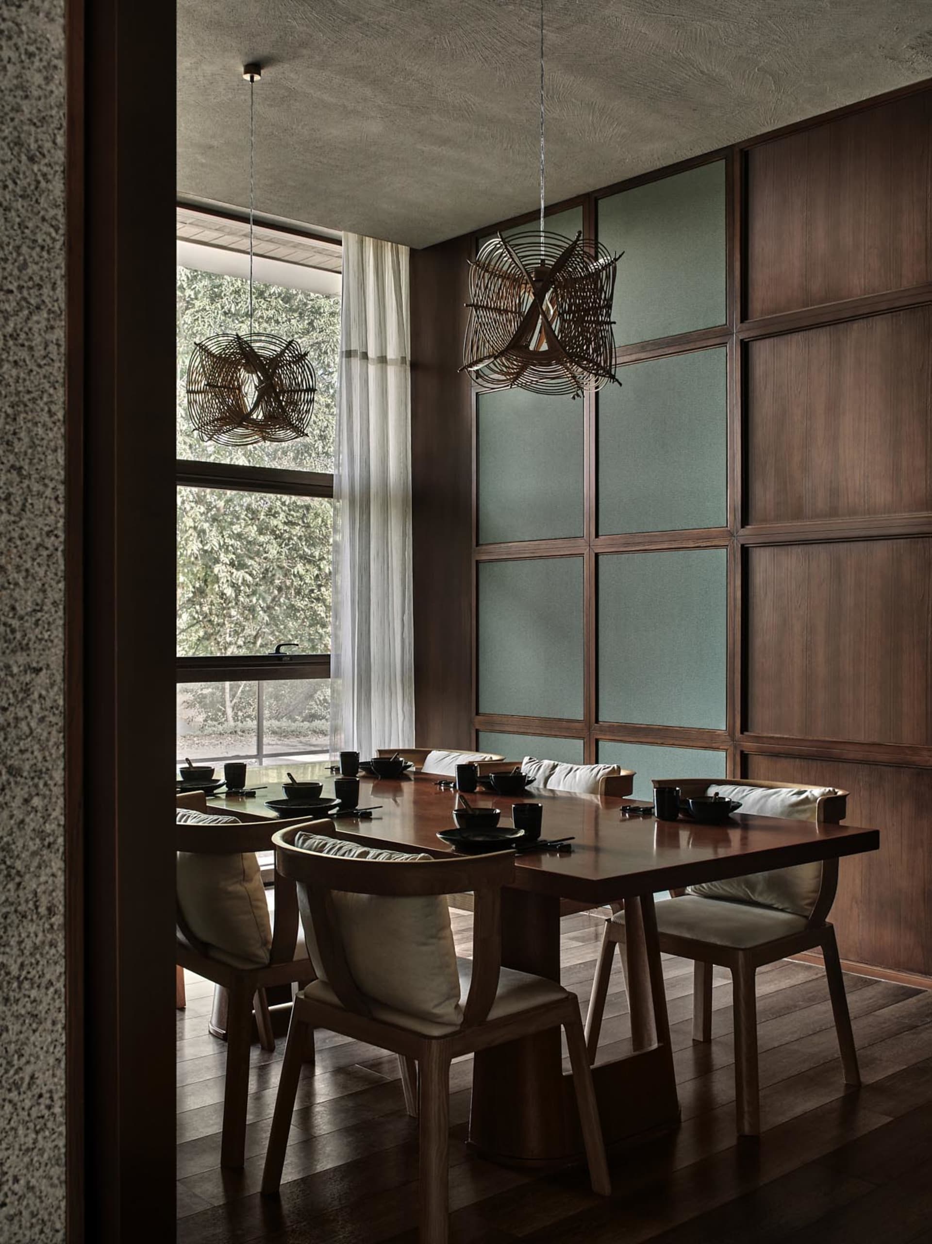 A minimalist dining room with wooden furniture and a large window showing greenery.