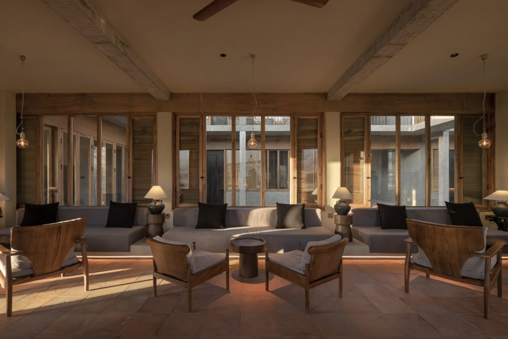 Modern minimalist living room with concrete floors, wooden furniture, and floor-to-ceiling windows.