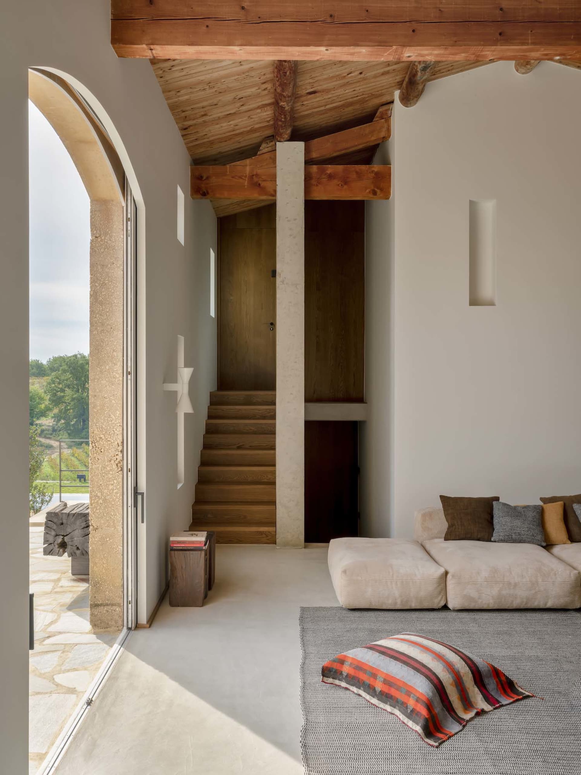 A modern living room with concrete walls and a wooden staircase leading to an upper floor.