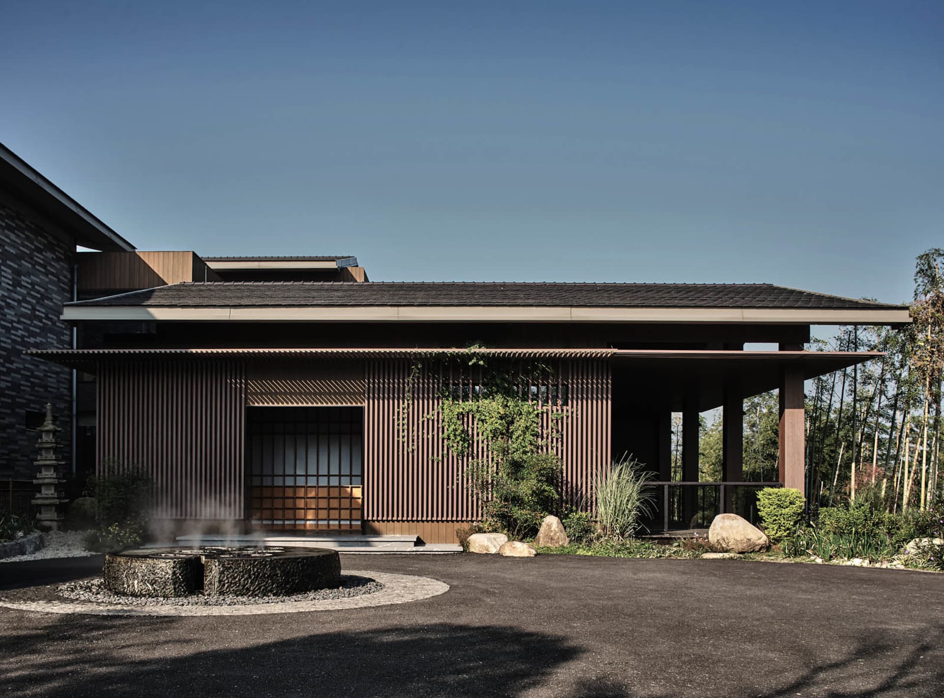 A modern residential building with wooden beam roof and lush greenery around it.
