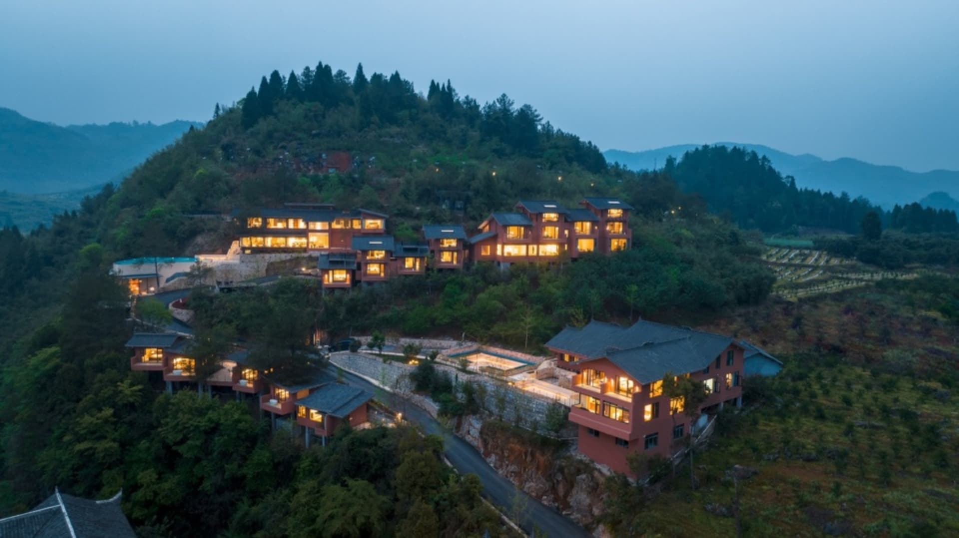 Modern residential buildings with lights on, situated on a hillside.
