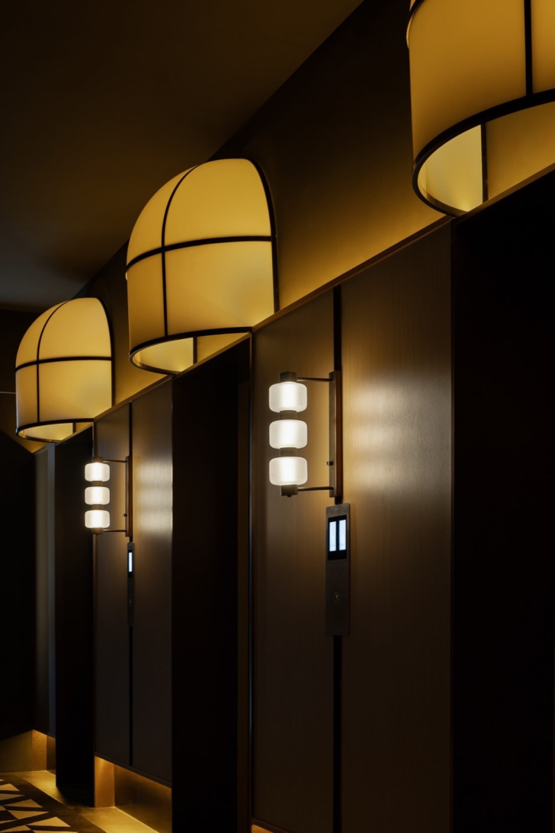 Well-lit elevator hall with modern lighting fixtures and dark wooden panels.