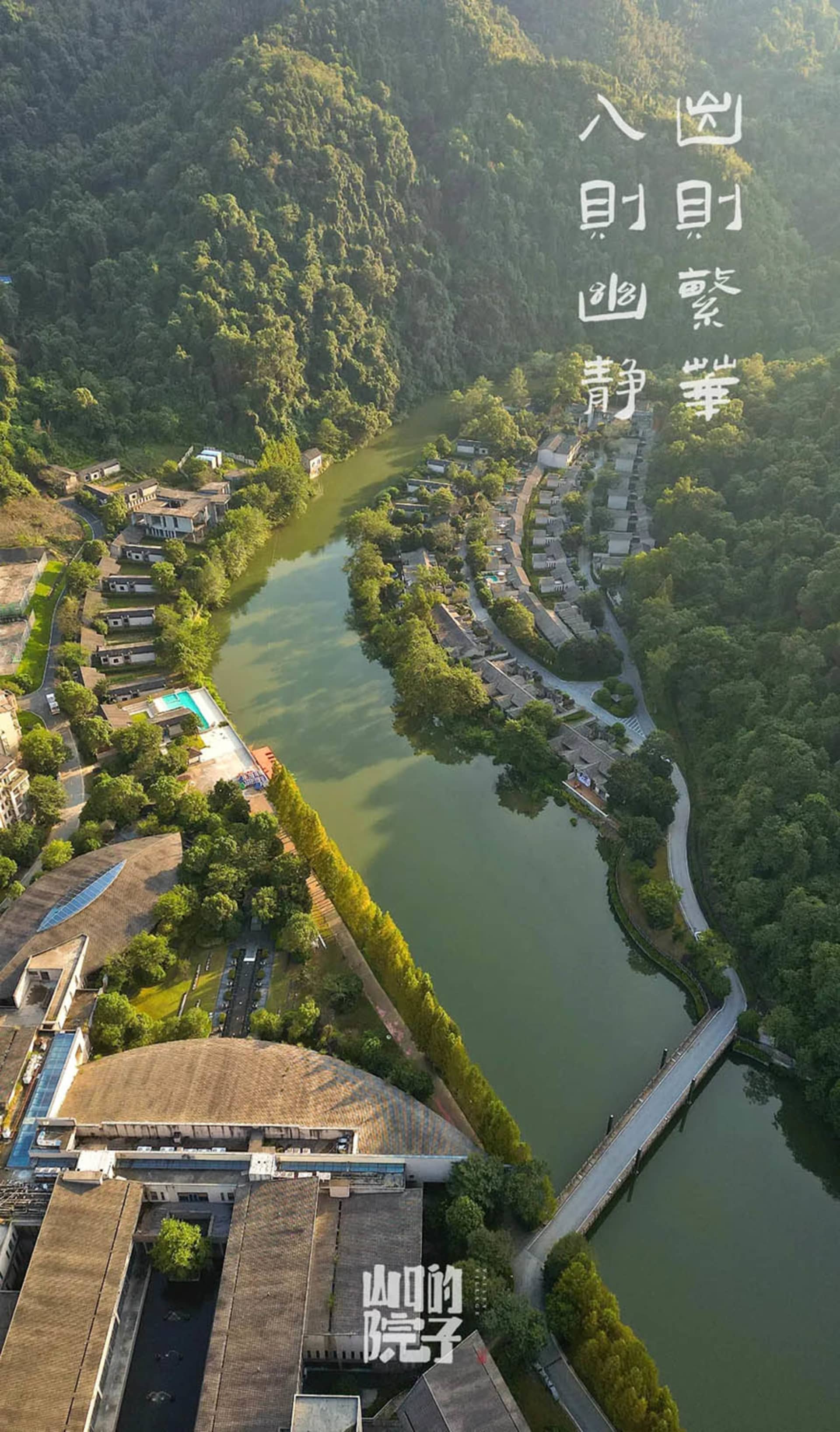 Aerial view of residential houses and buildings surrounded by lush greenery and a meandering river.
