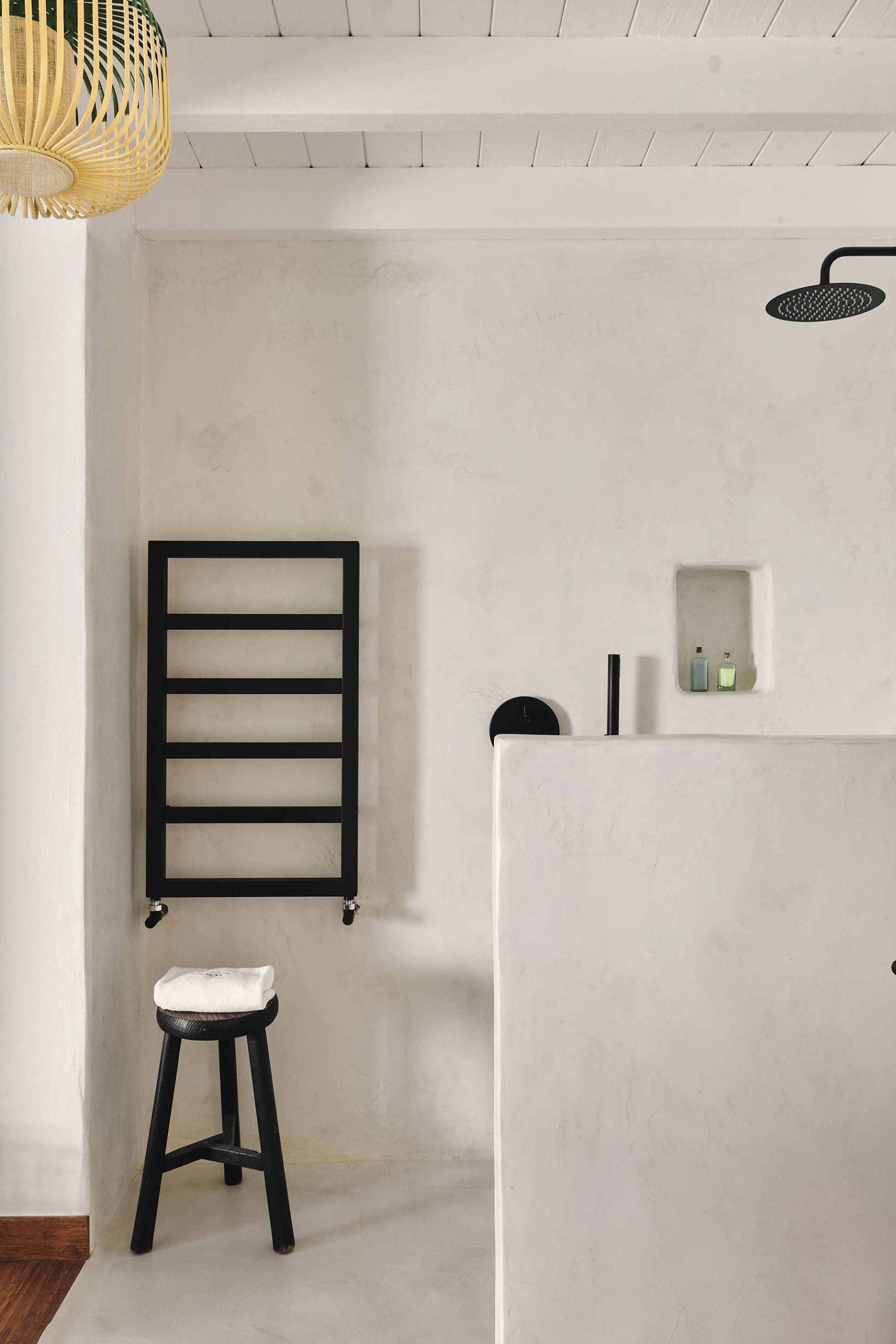 A minimalist bathroom with a concrete floor, wooden stool, and black towel rack.
