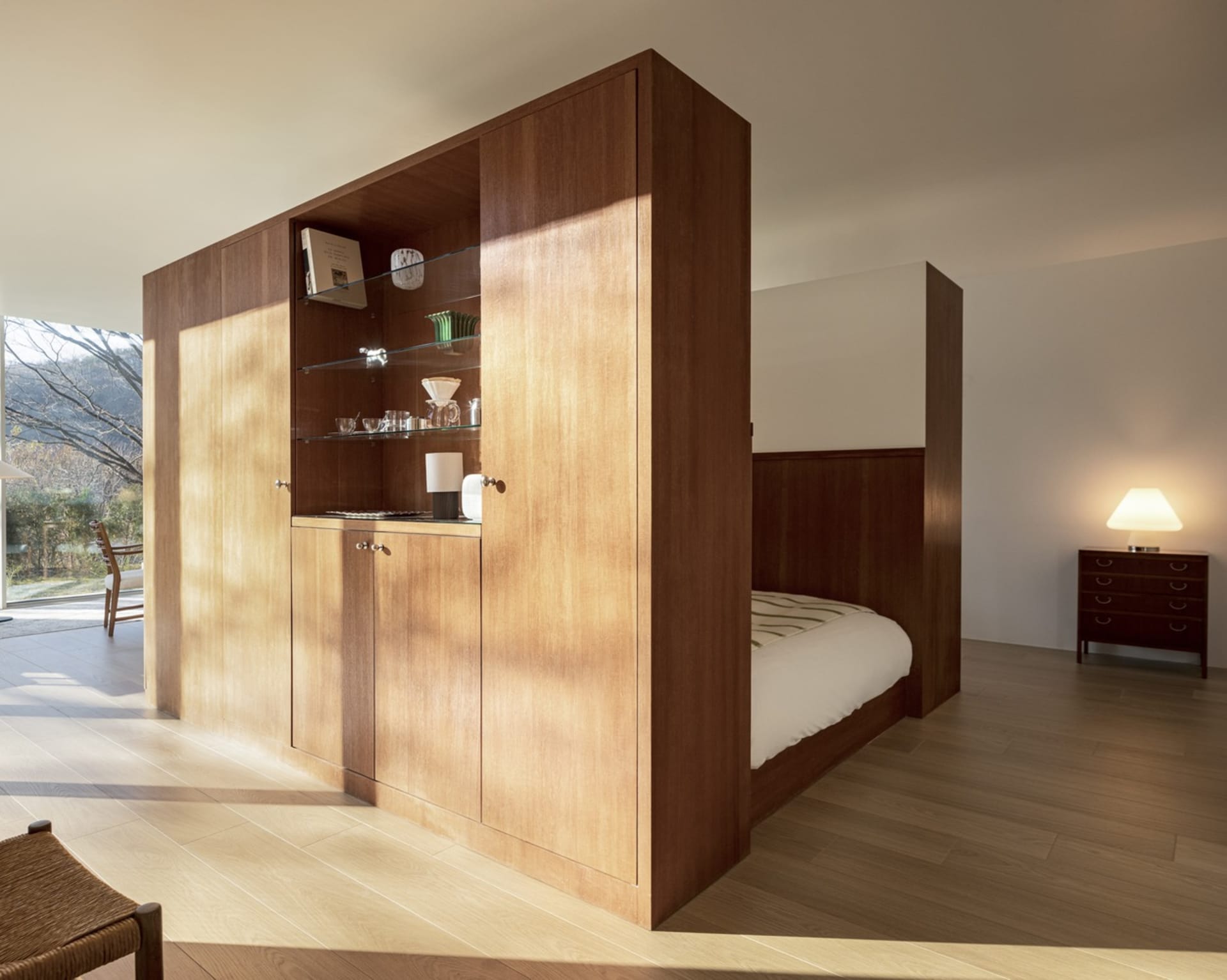Modern minimalist bedroom with wooden cabinets, glass shelves, and a bed.