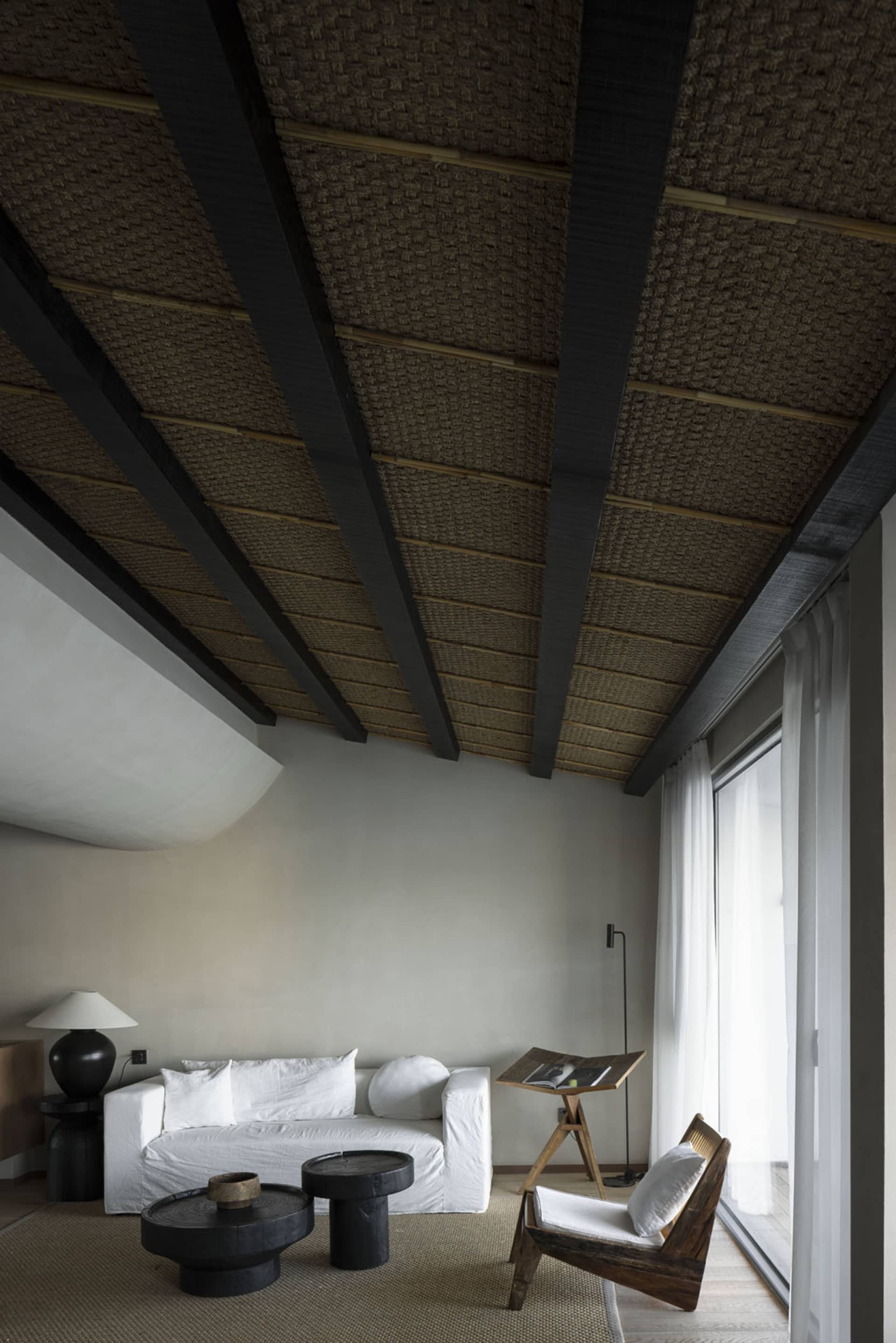 A minimalist lounge featuring a white sofa, wooden coffee tables, and a wooden armchair.