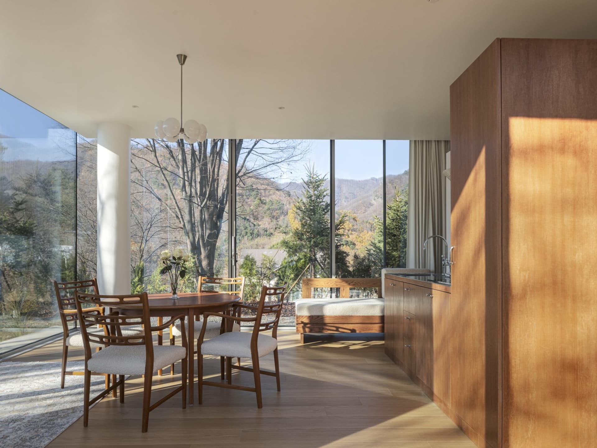 A minimalist residential kitchen featuring wood elements and a view of the mountains through floor-to-ceiling windows.