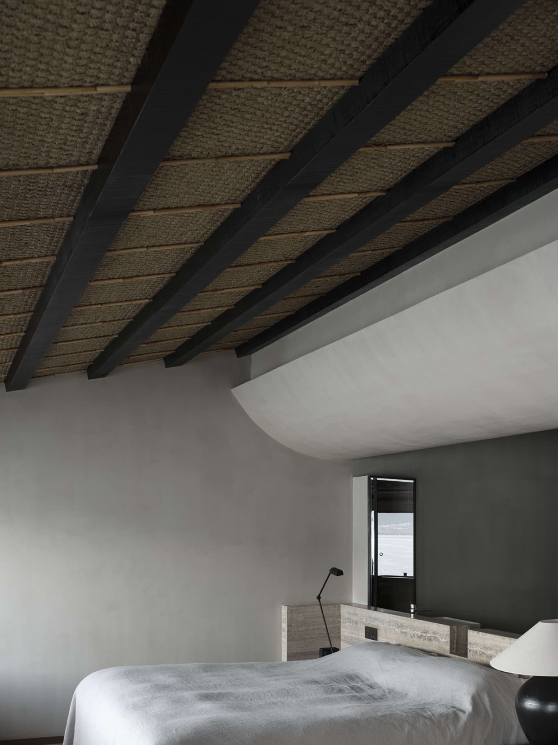 Interior of a modern minimalist bedroom featuring a concrete finish and a view of the ocean through a window.