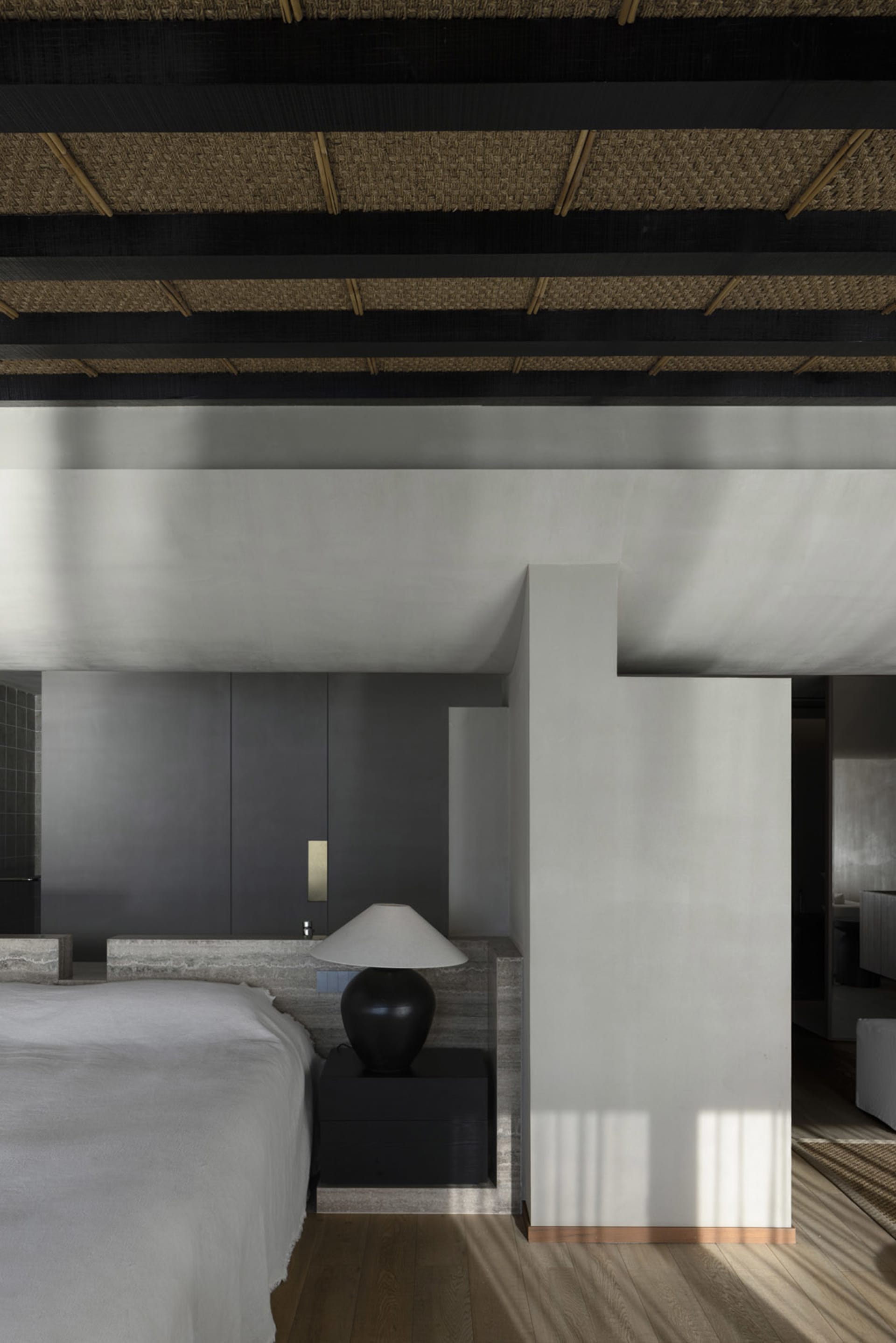 A modern minimalist bedroom featuring a large bed with a concrete frame and a black lamp on a nightstand.