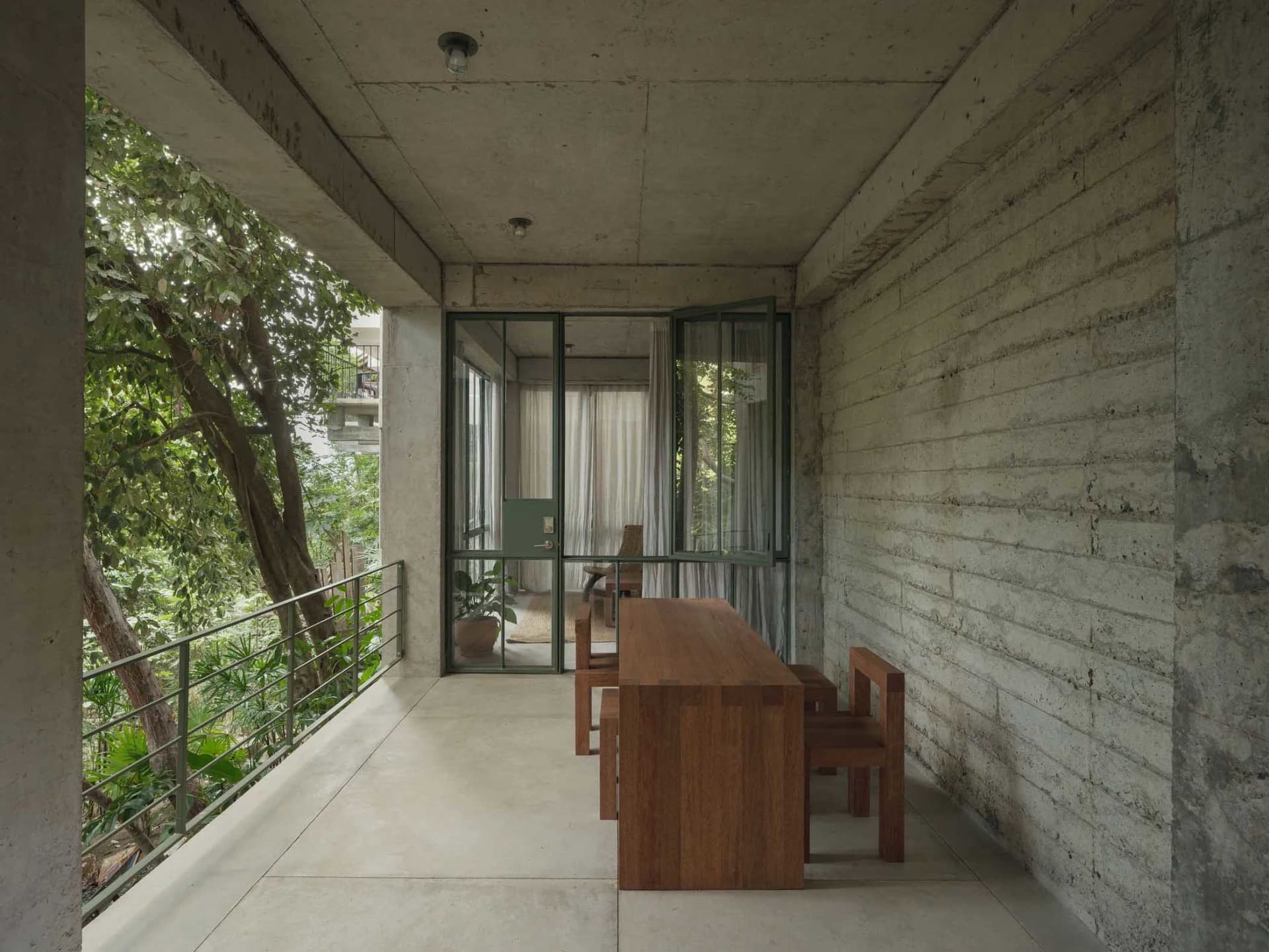 Concrete patio with minimalist furniture and lush greenery surrounding it.