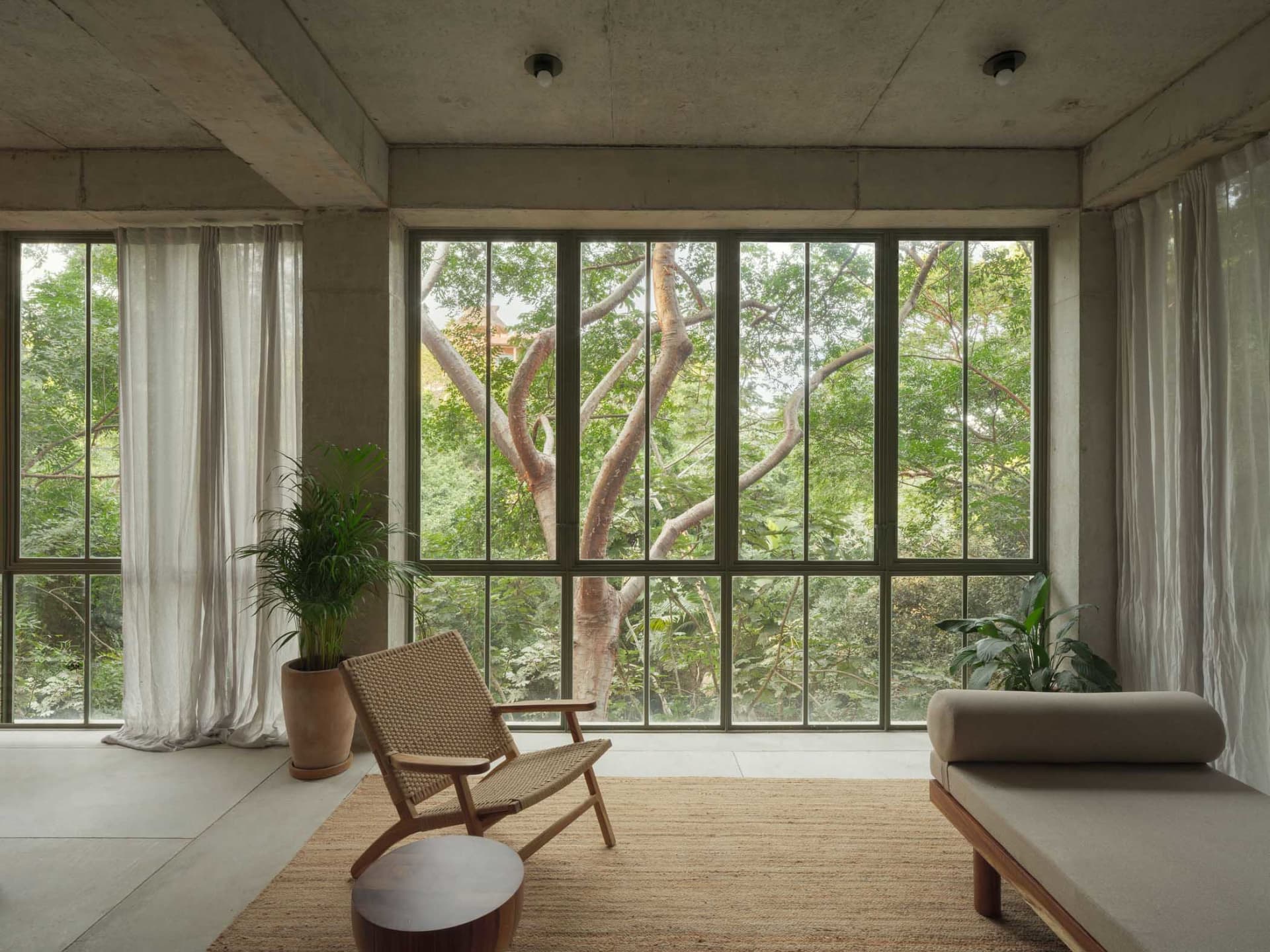 A minimalist living room with concrete walls, large glass windows, and fabric furnishings.