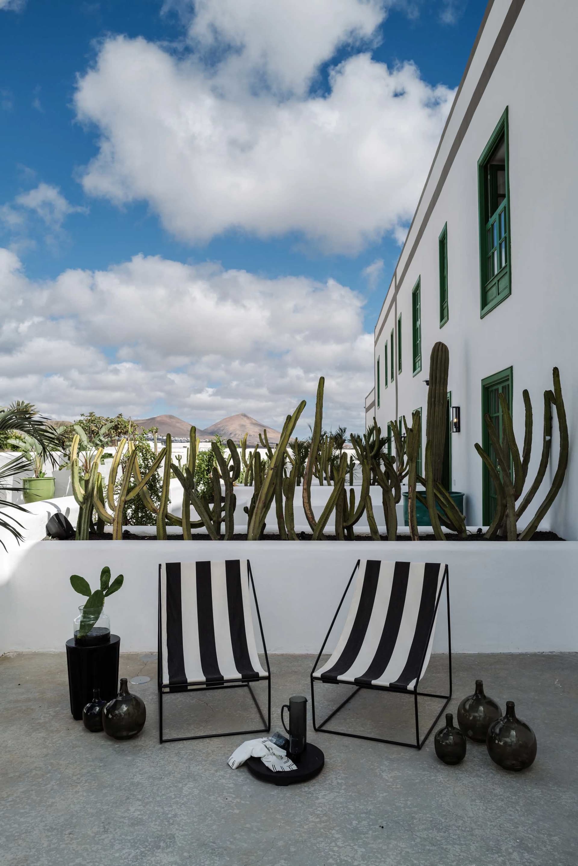 Modern patio with black and white striped chairs, concrete walls, and greenery.
