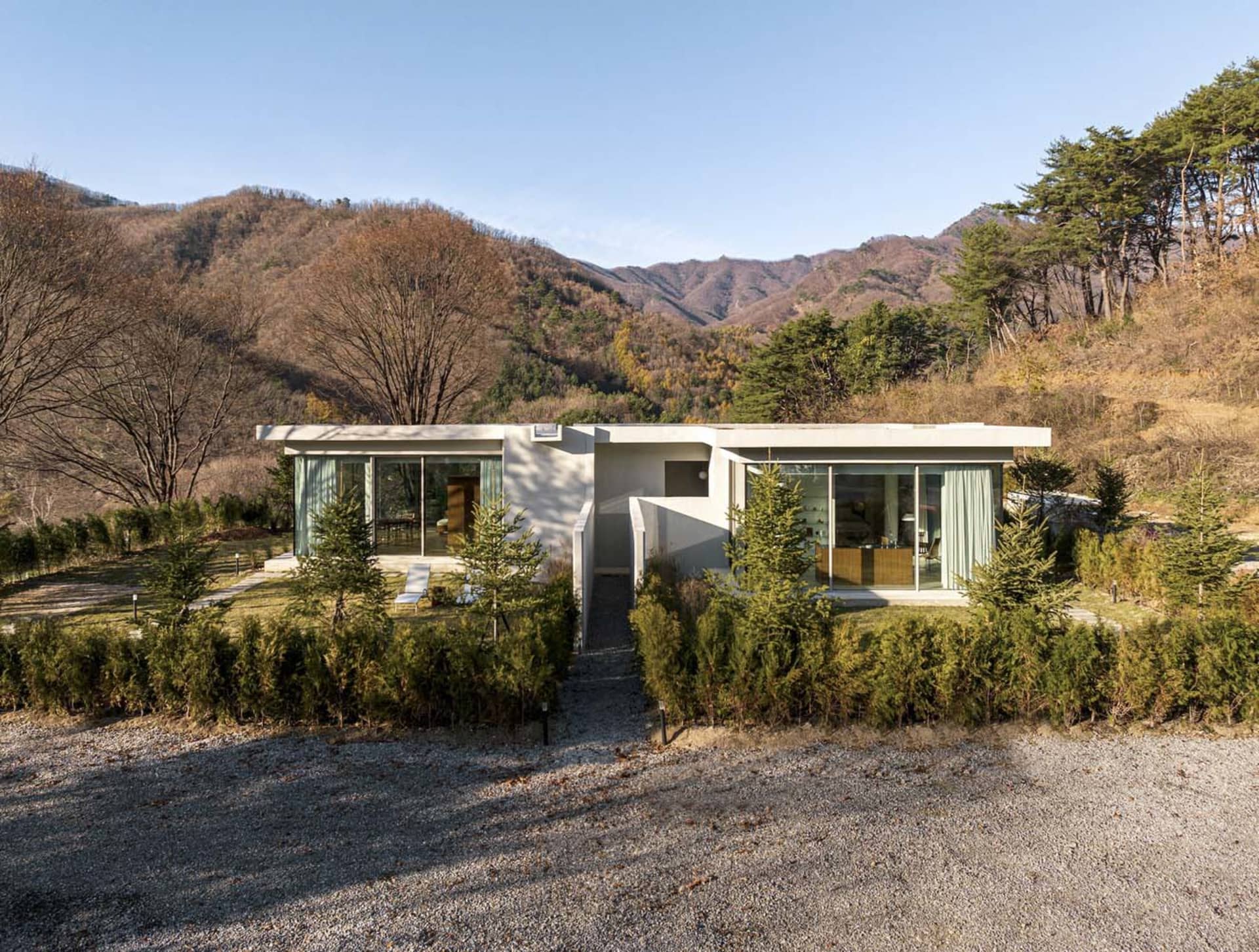 A modern residential house with large glass windows and a concrete exterior surrounded by a landscaped garden with trees and