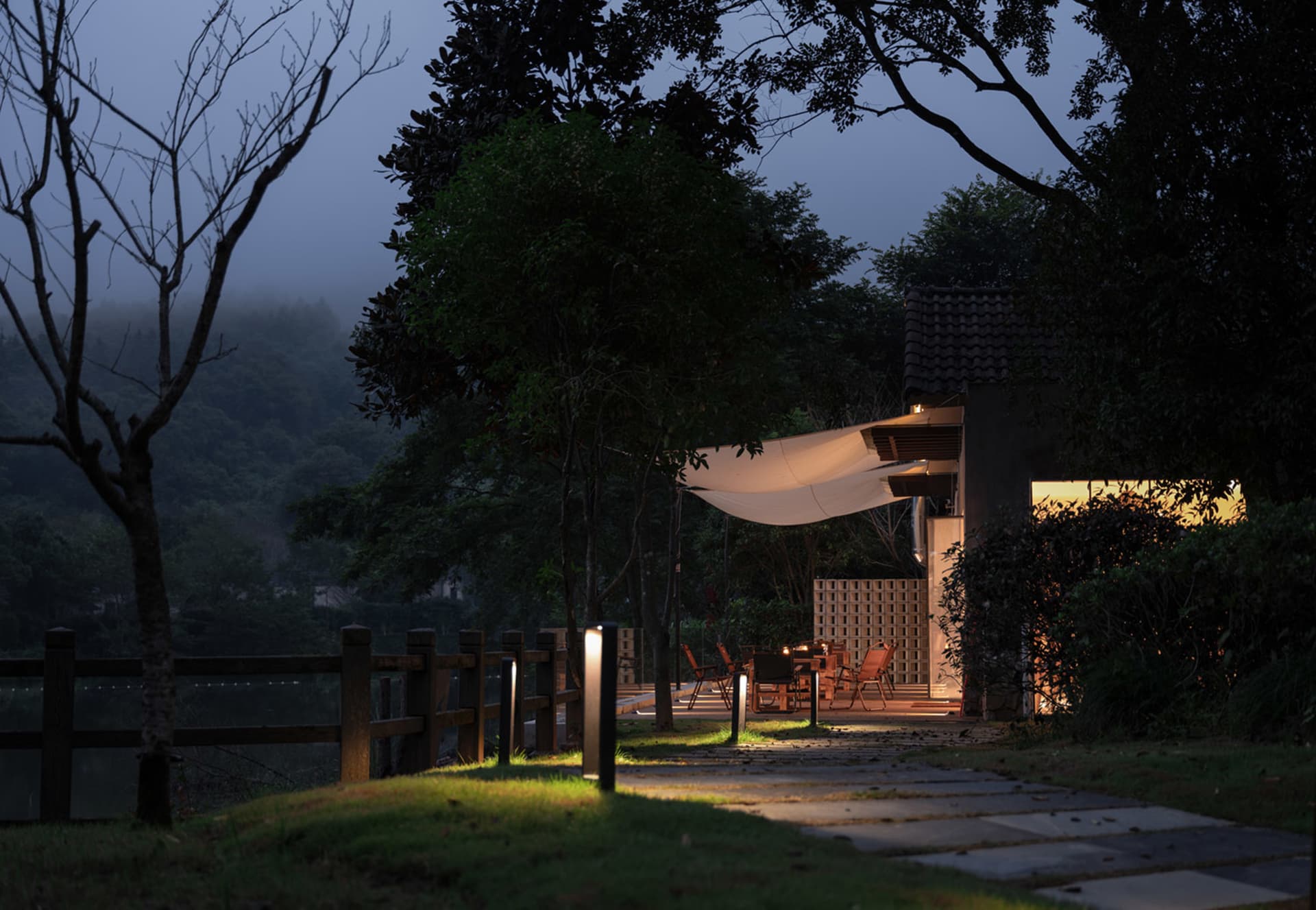 A night-lit backyard patio with wooden flooring, fabric awning, and metal patio furniture.