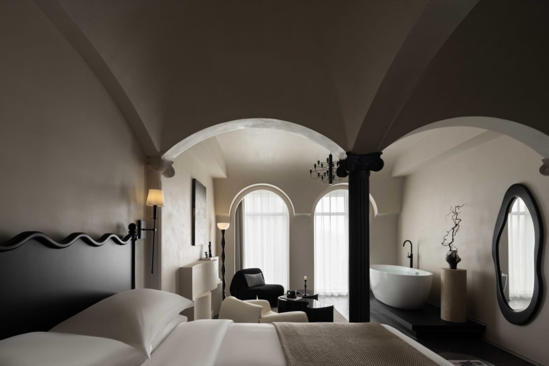 A minimalist hotel bedroom featuring white marble surfaces and black metal furniture.