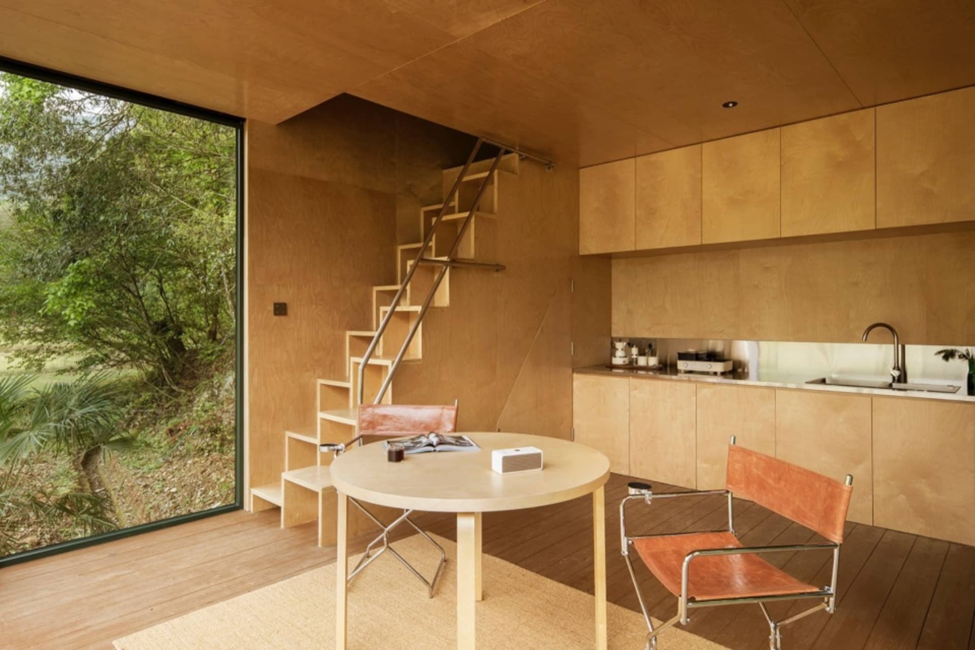 Minimalist kitchen with a natural wood finish, featuring a round table and chairs, a kitchen counter with cabinets, and a lad