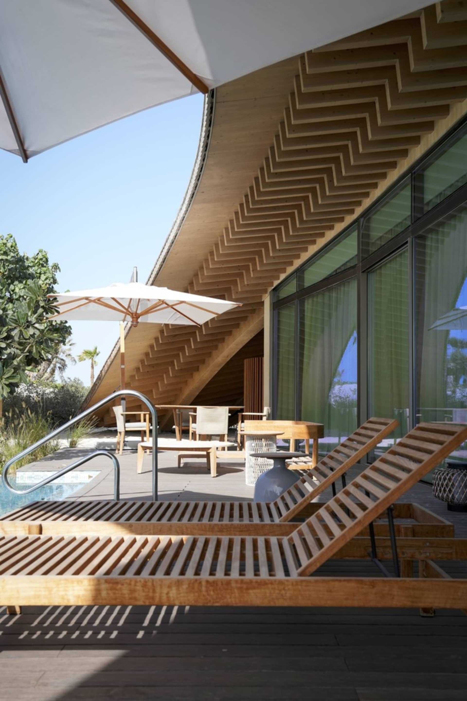A modern patio with a swimming pool and wooden furniture and stairs.