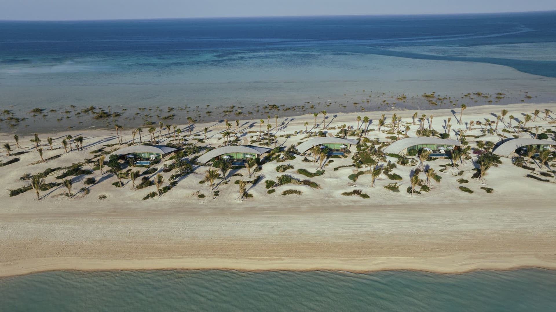 Aerial view of modern buildings on a sandy beach with clear blue waters.