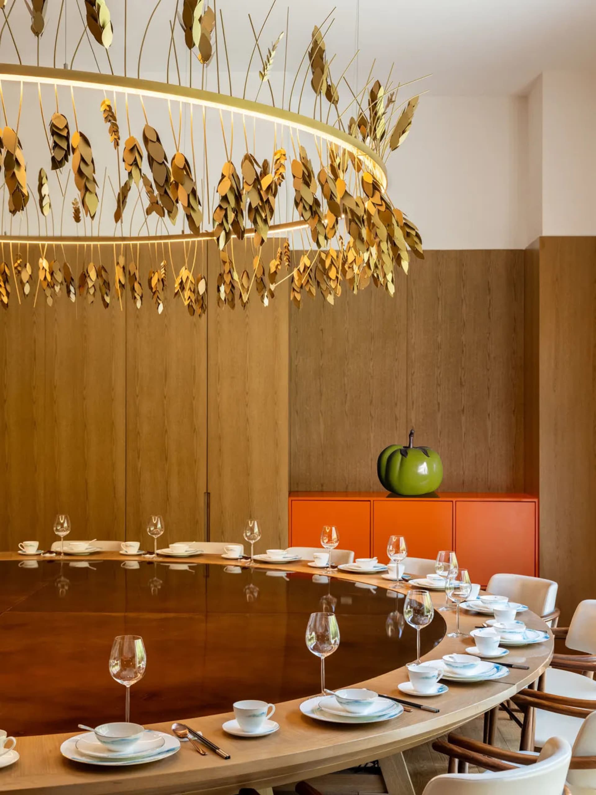 A modern restaurant interior with wooden furniture, featuring a large round table set for dining, a golden chandelier hanging