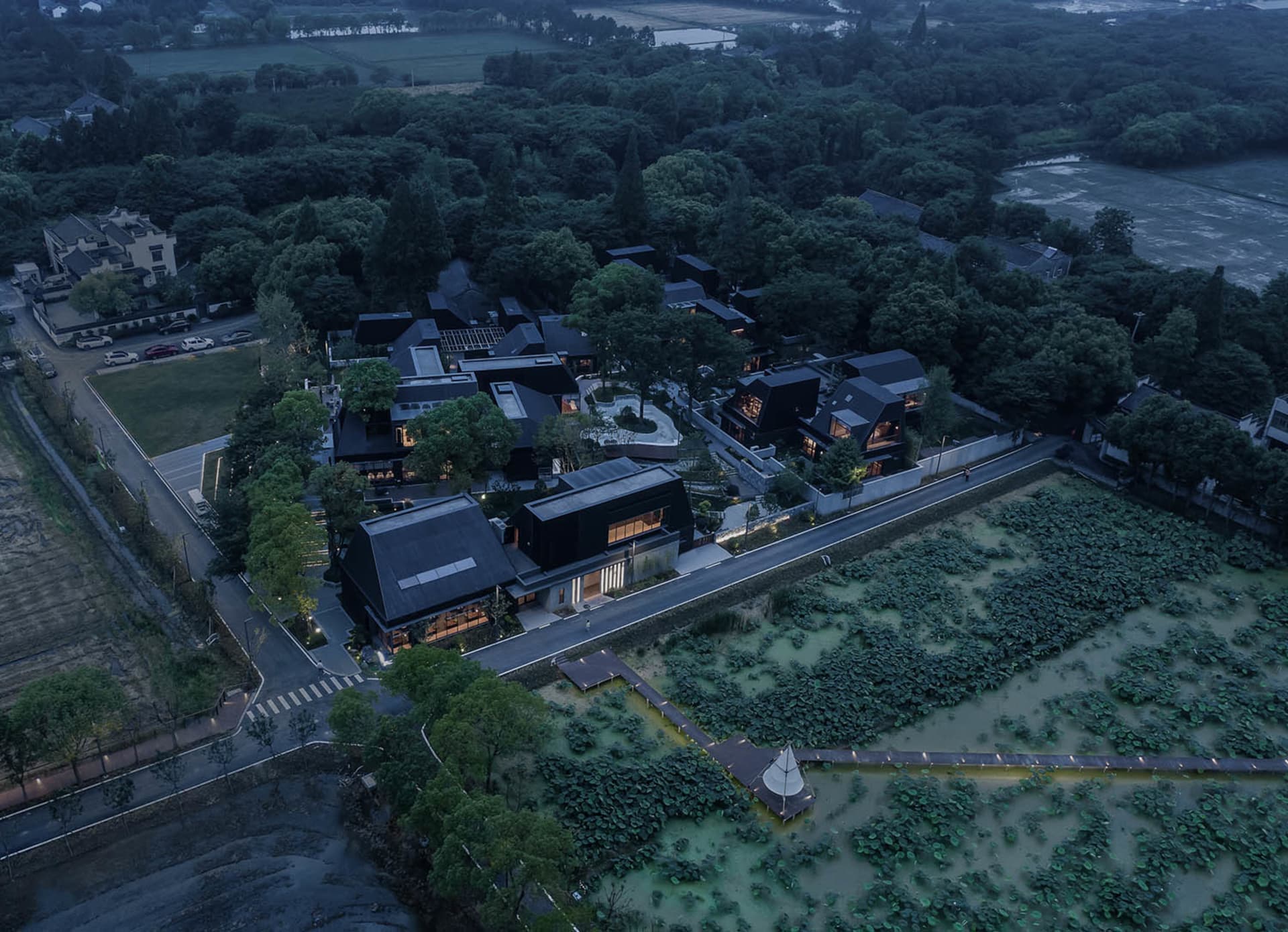 俯瞰現代黑屋頂住宅，綠意環繞，室內燈光與花園區域映入眼簾。