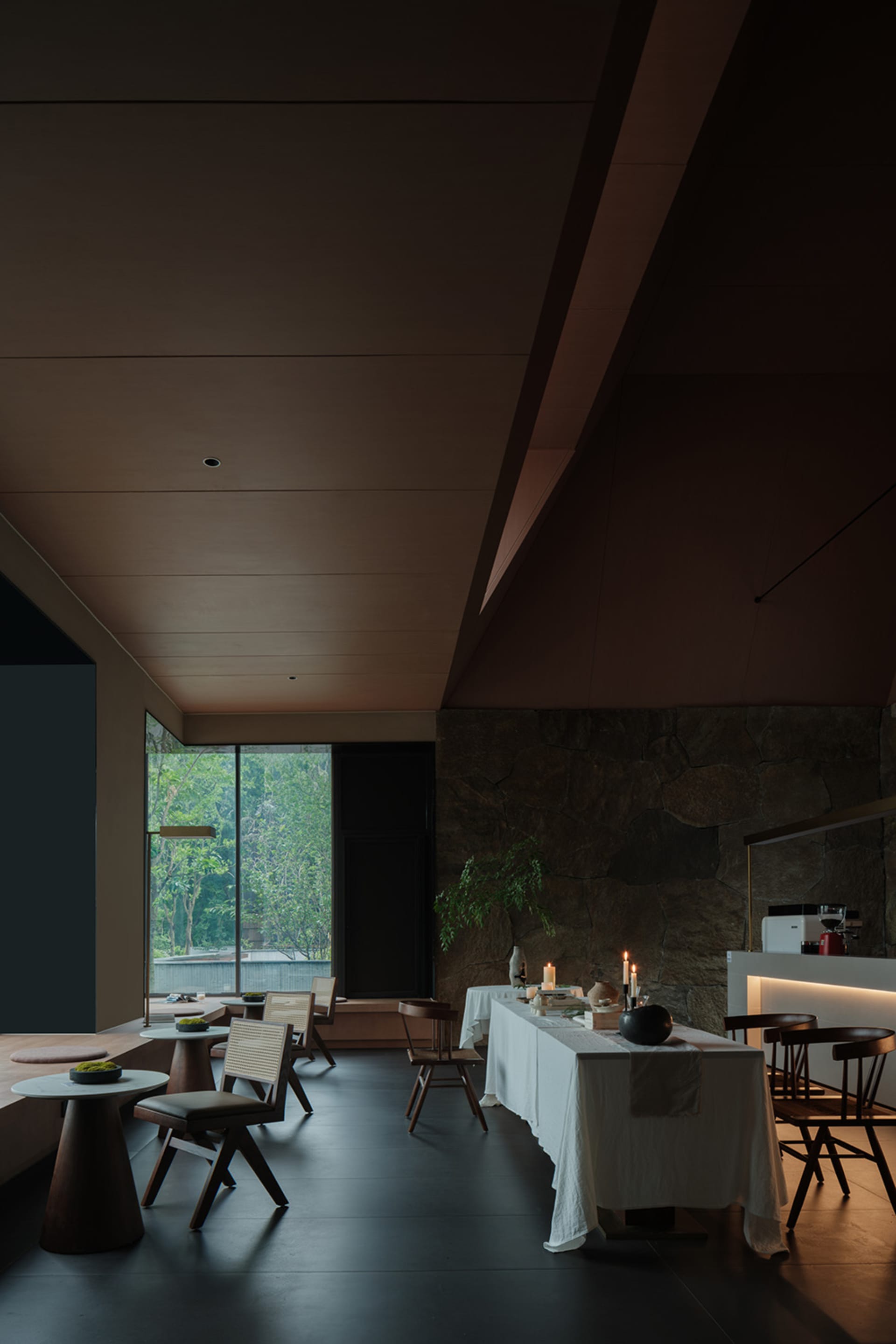 A modern restaurant dining room featuring stone flooring, sleek furniture, and natural light.