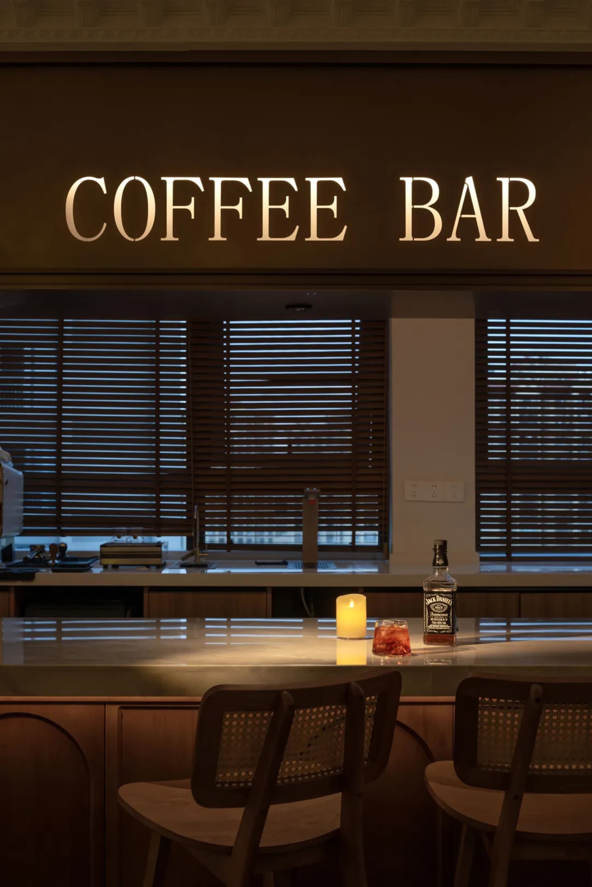 Modern coffee bar with illuminated counter and wooden chairs.