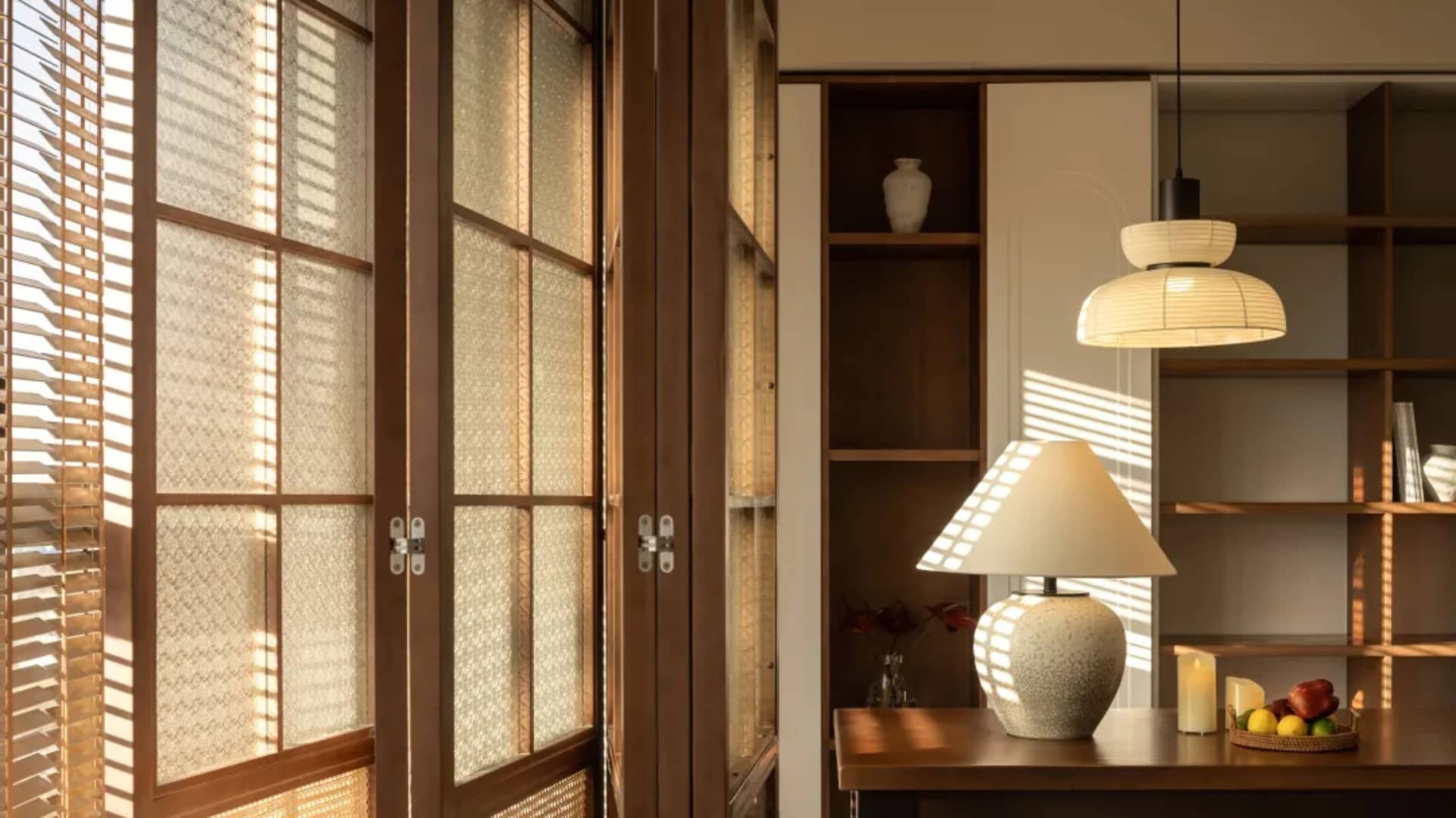 一間光線充足的客廳,鋪設木質地板,並設有木製餐桌,桌上擺放燈具與裝飾品。