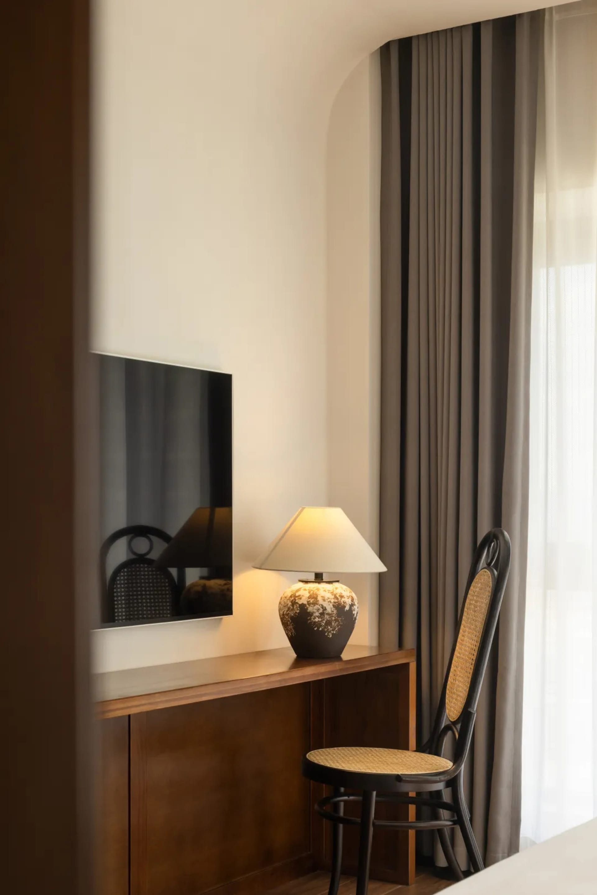 A modern workspace featuring a wooden lamp with a white shade, a black steel and canvas chair, and a flat-screen TV on a buil
