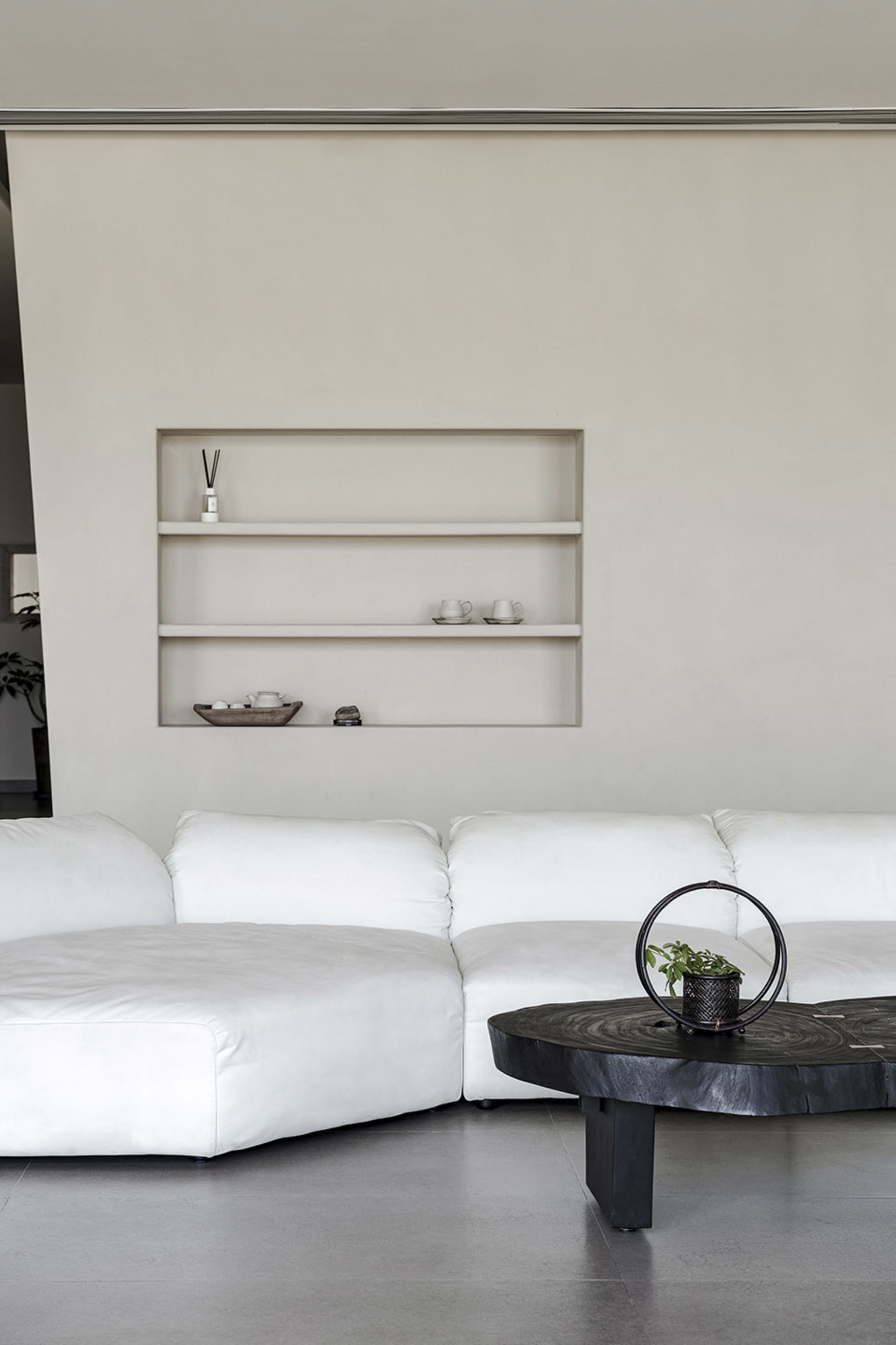 A minimalist living room with a large white sofa and a black coffee table on a concrete floor.