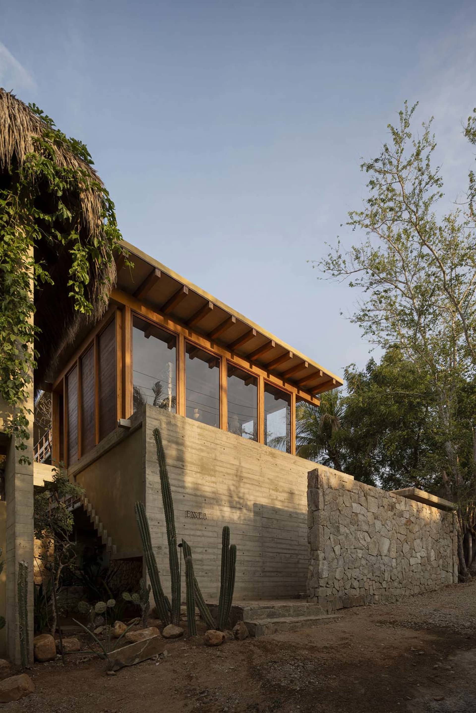 Modern residential house with concrete walls, stone foundation, and thatched roof.