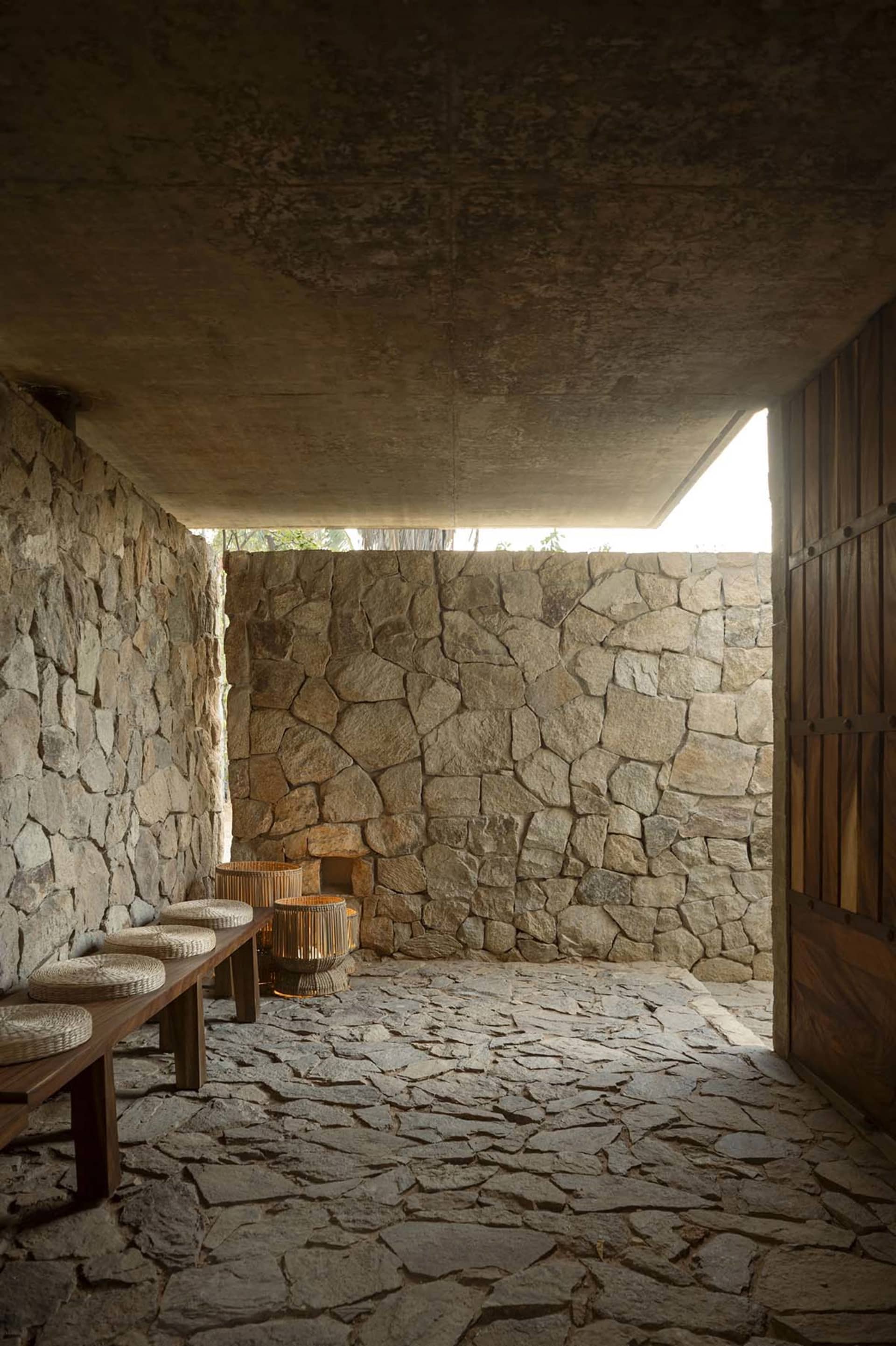 A stone-walled interior with wooden furniture and baskets on a stone-paved floor.
