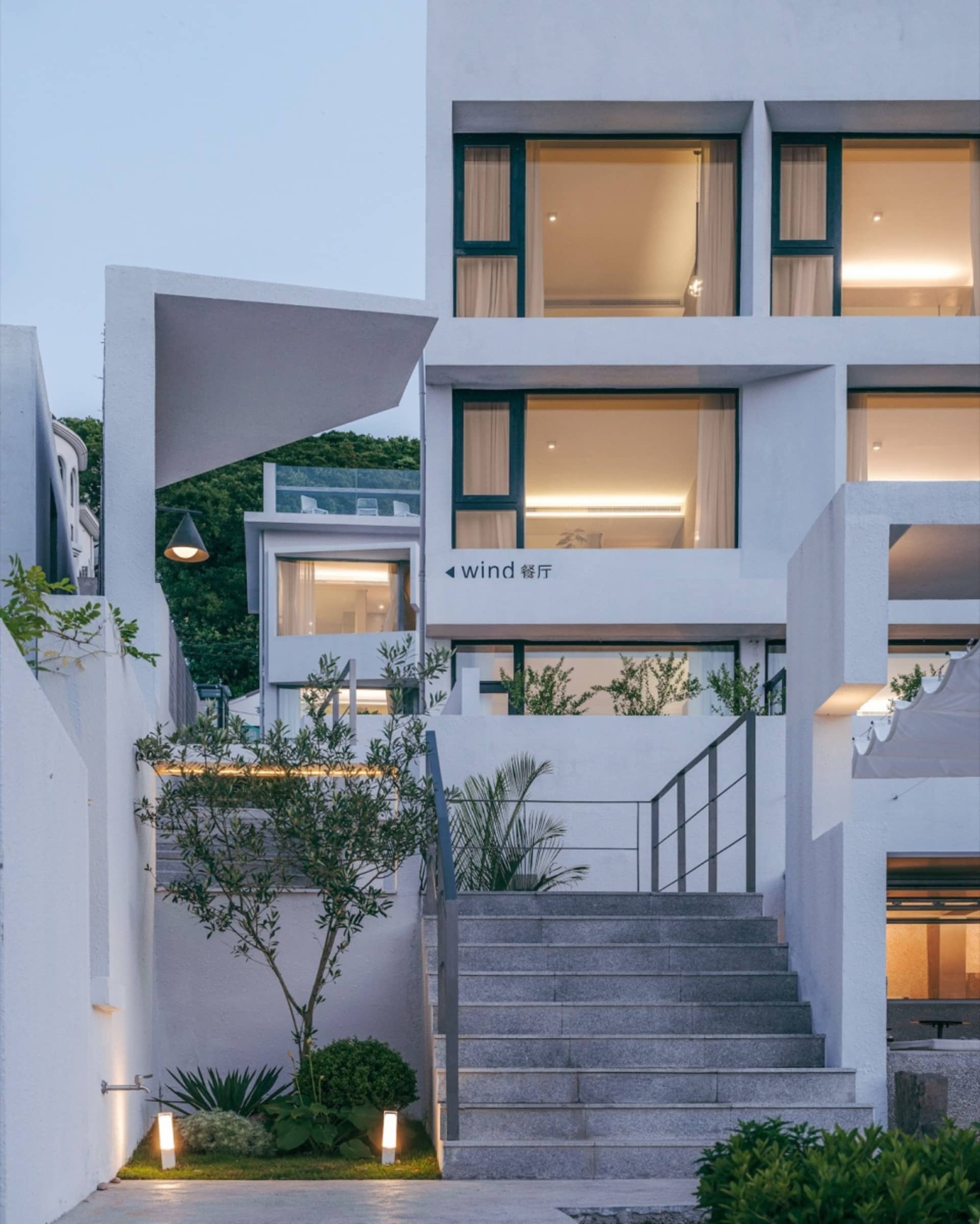 Modern building with concrete and glass exterior, metal railings and greenery.