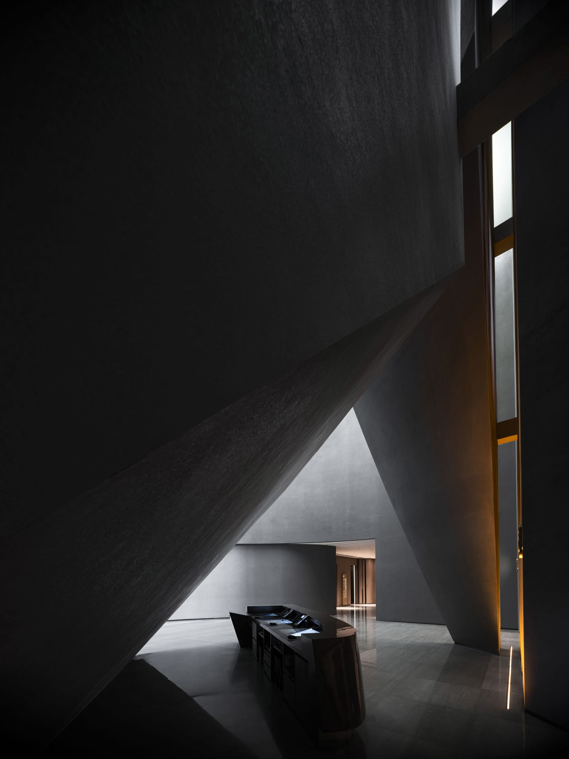 A minimalist hotel reception area with concrete walls and a sleek, black reception desk.