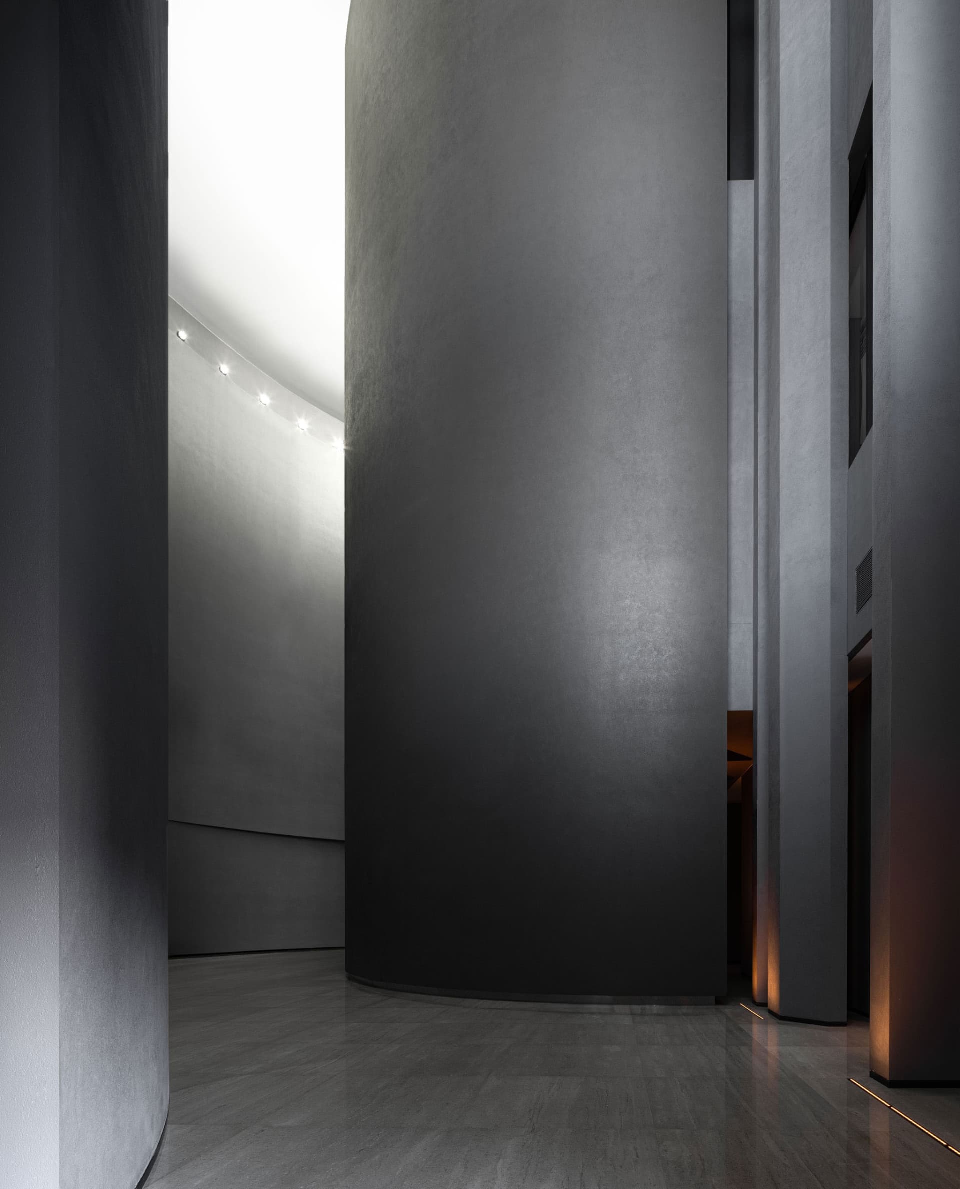 A modern, minimalist interior space with a textured concrete wall and floor, illuminated by recessed lighting.
