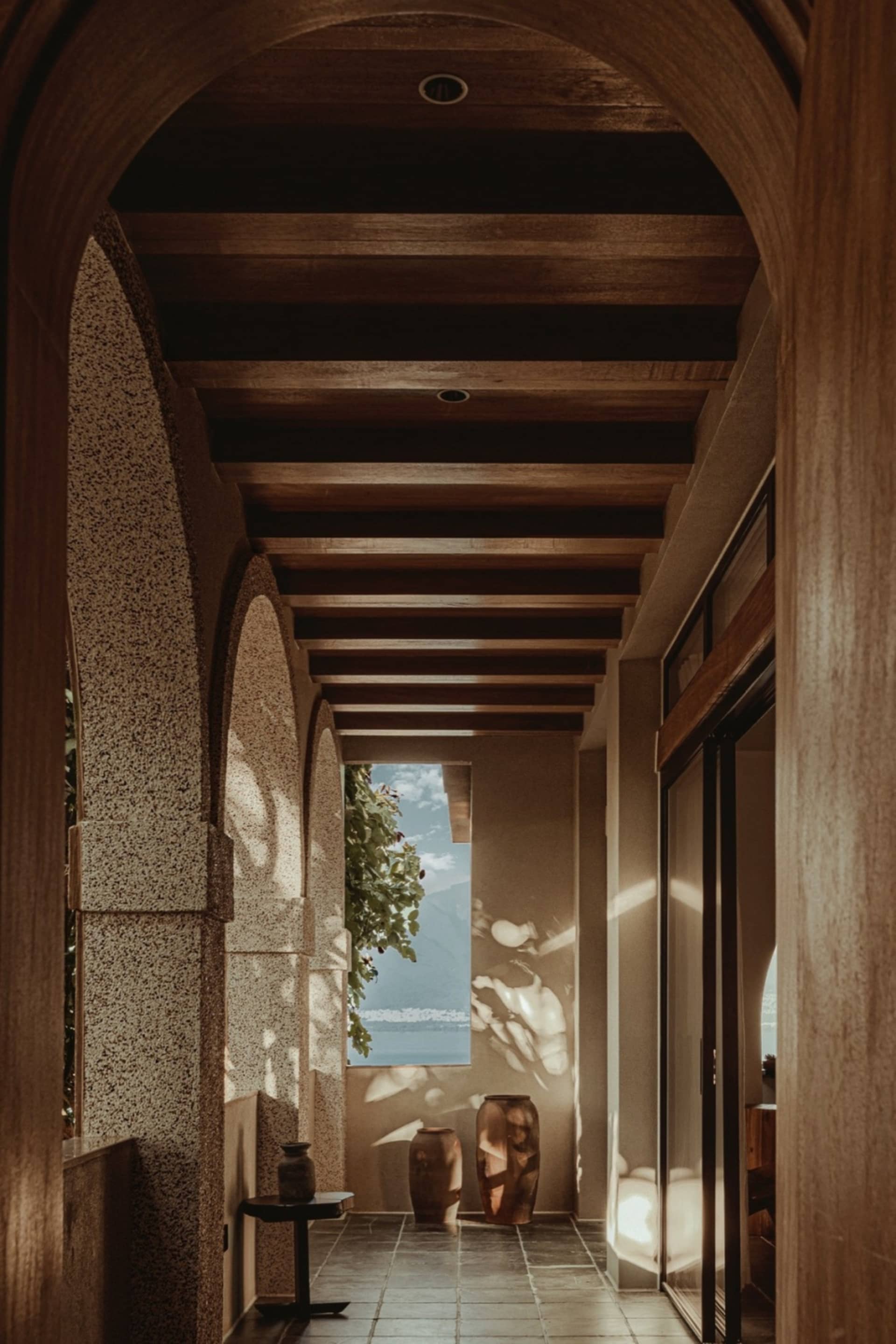 Modern residential interior featuring a corridor with arches, a terrazzo floor, and wooden beams on the ceiling.