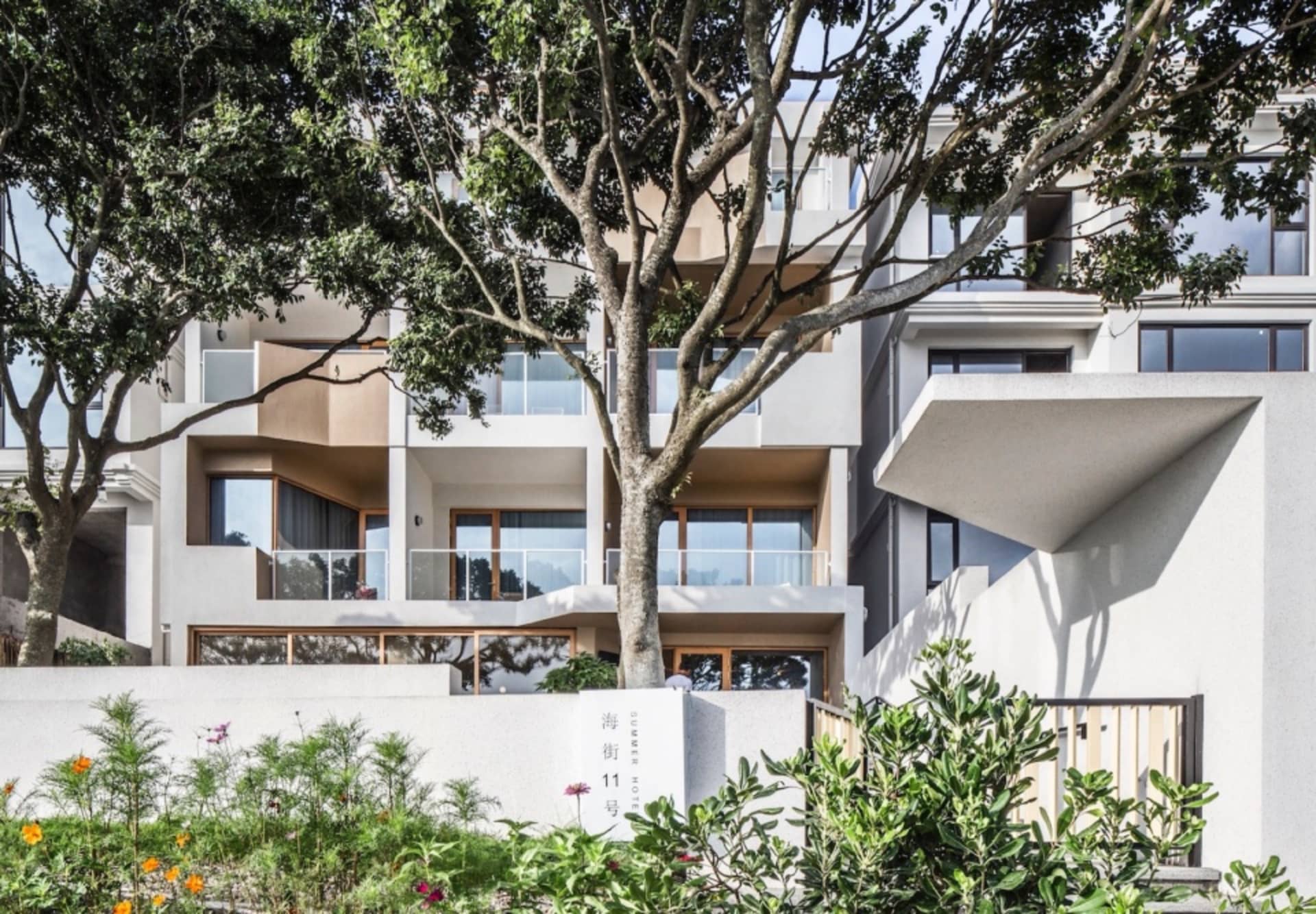 一座現代住宅建築,擁有砂岩外牆,前景有大型樹木。