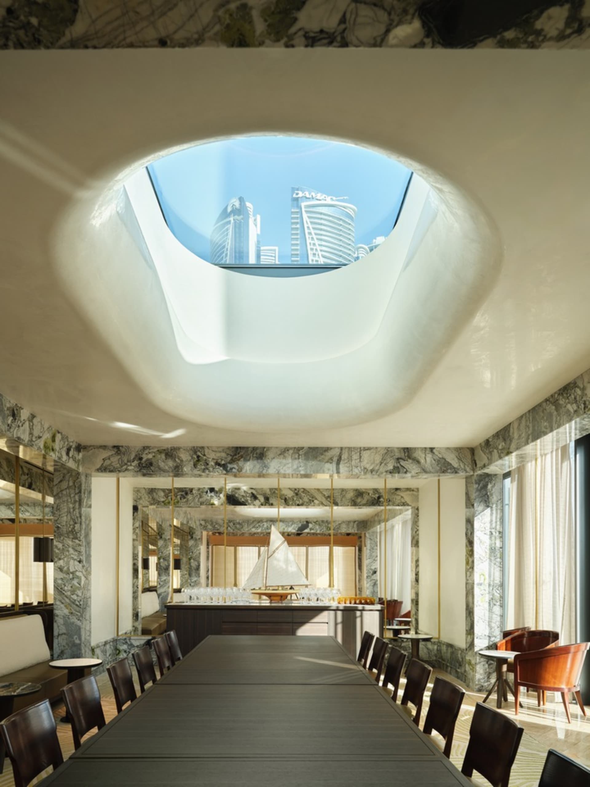A modern restaurant interior with marble walls and a large skylight.
